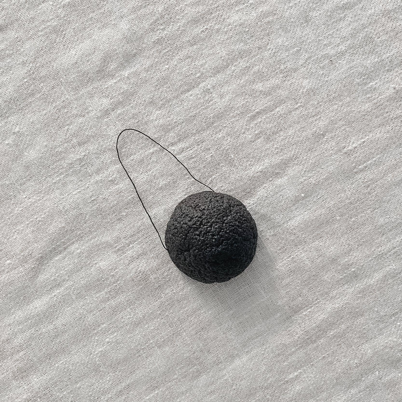 The Grace & Company Meraki Konjac Sponge, round and black with a string, sits on a light textured surface.