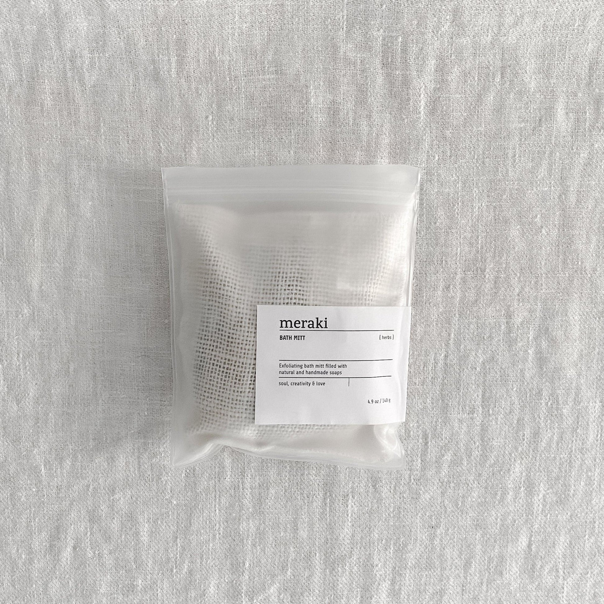 Grace & Company Meraki - Bath Mitt in a clear bag on textured white fabric.