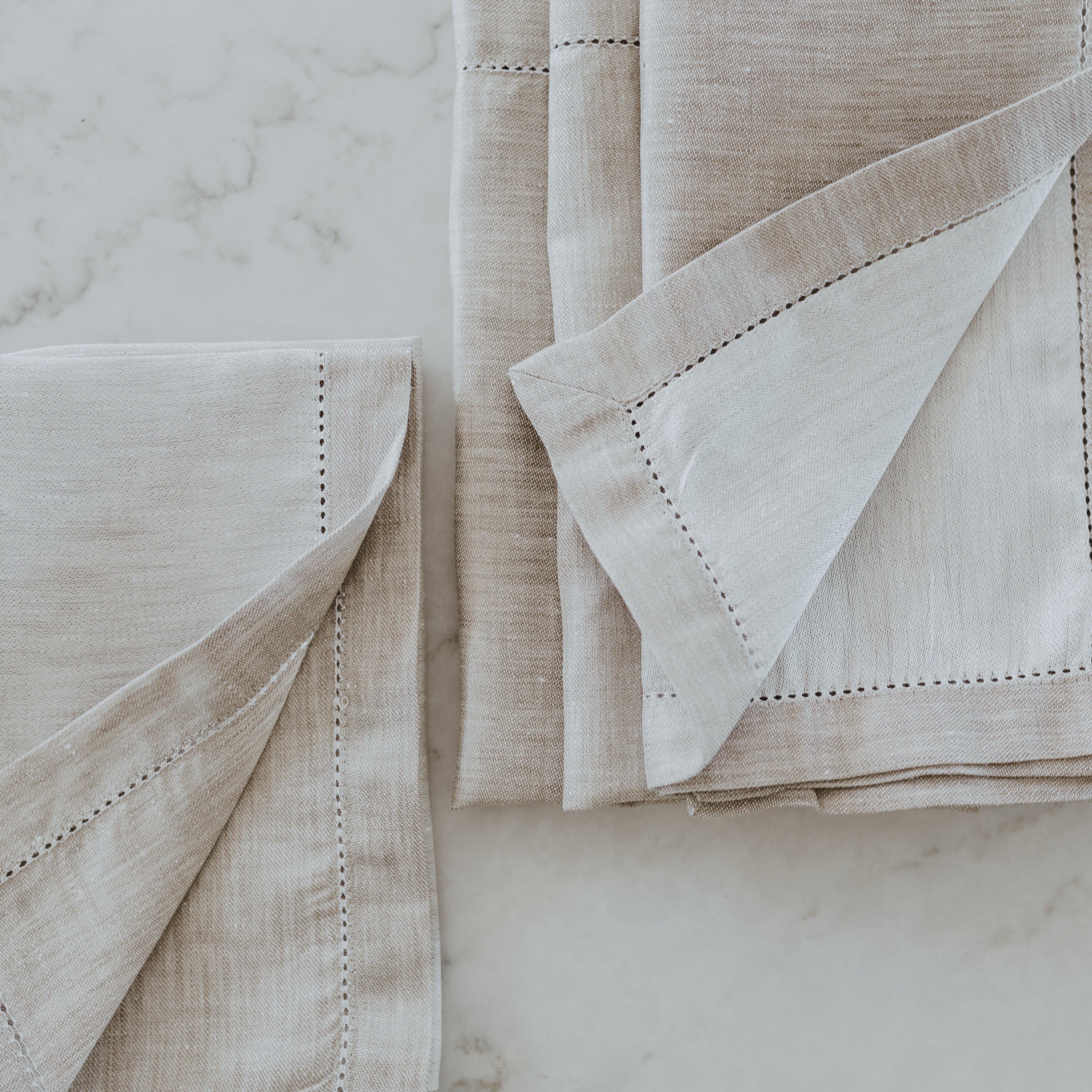 Grace & Company Linen Way - Versailles beige napkins with decorative stitching on white marble.