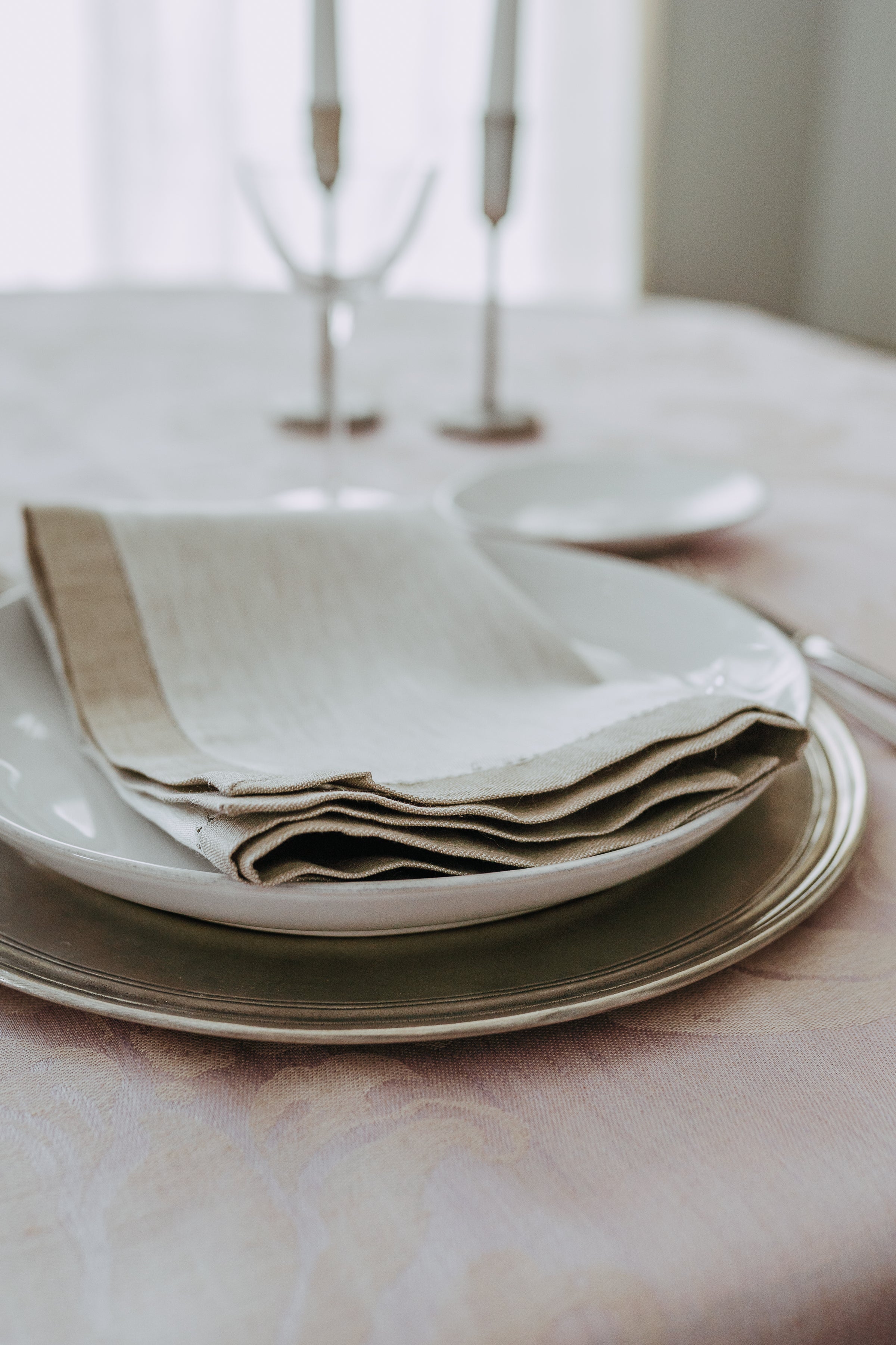 A close-up of Grace & Company’s Linen Way - Versailles Table Napkin folded on a white plate with soft, elegant lighting.
