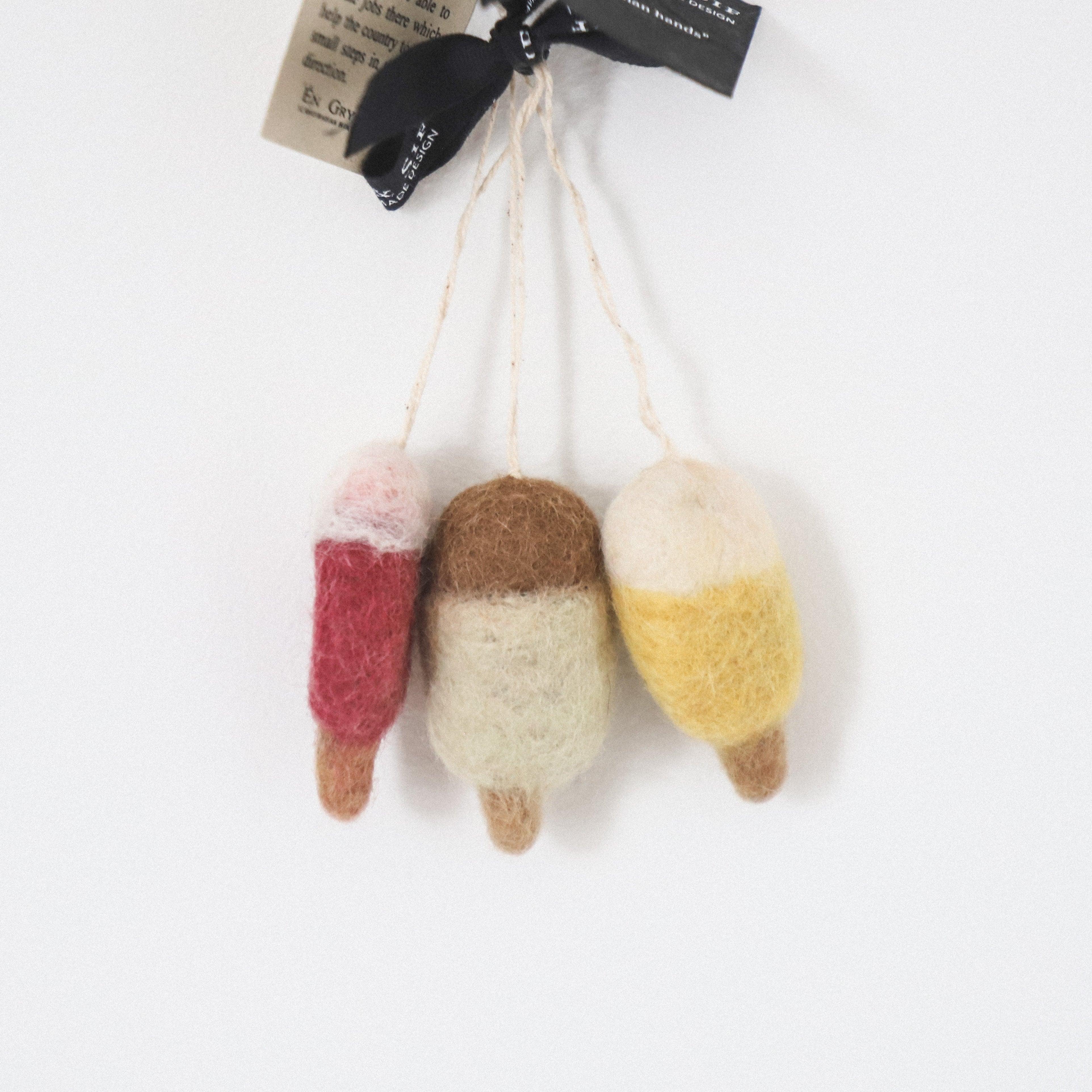 Three Scandi Wool Ice Lolly Ornaments by Grace and Company Ltd in red, brown, and yellow hang by strings.