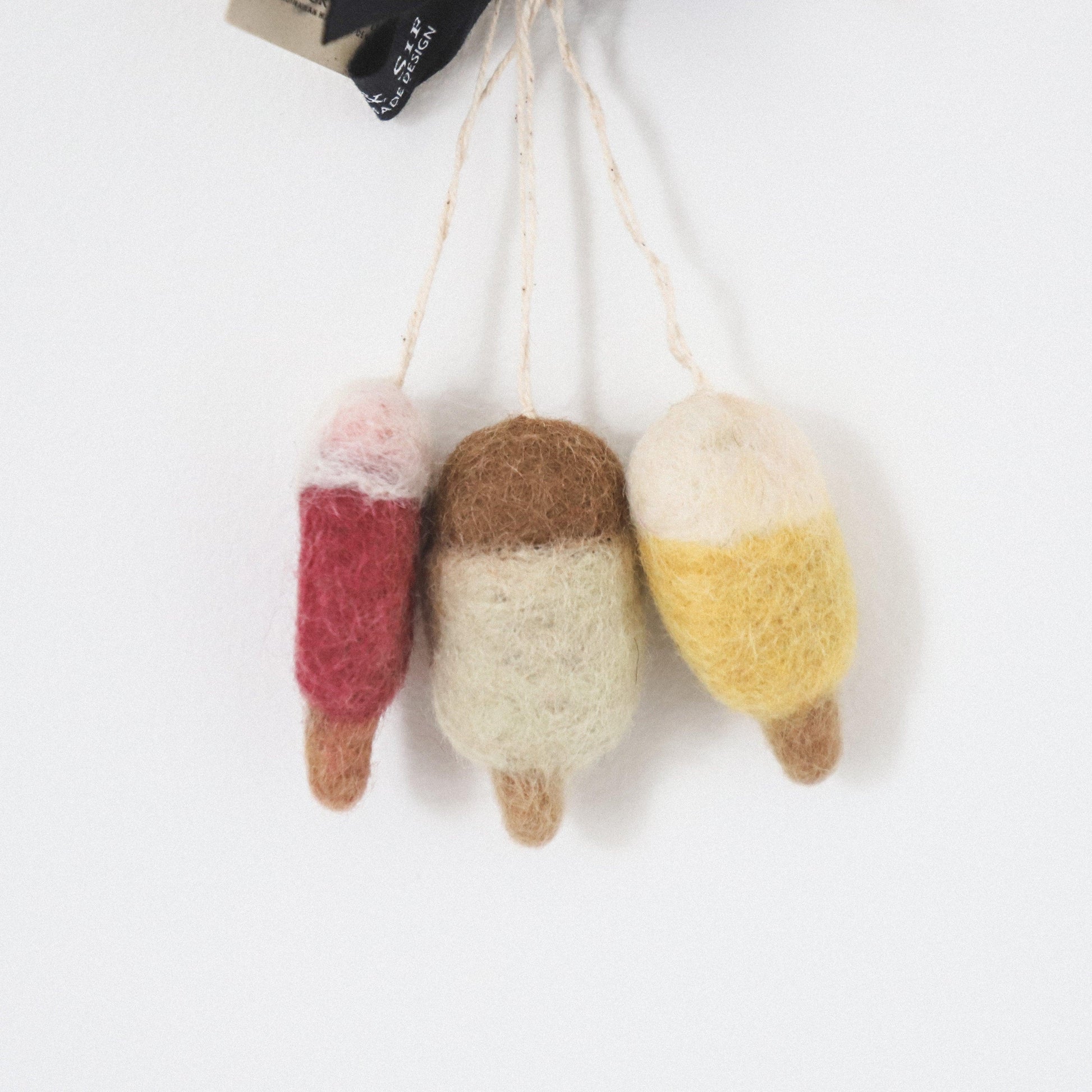 Three Scandi Wool Ice Lolly Ornaments by Grace and Company Ltd in red, brown, and yellow, hanging by strings.