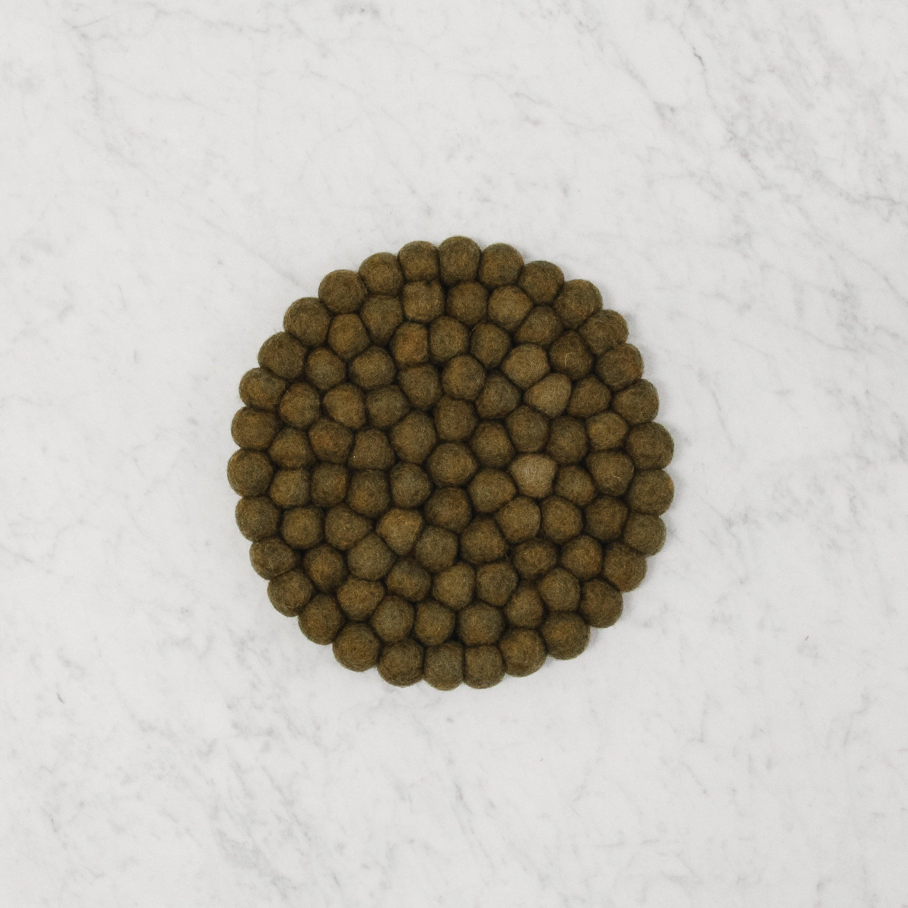 A round cluster of dark brown Grace & Company Felt Ball Trivet on a white marble surface.