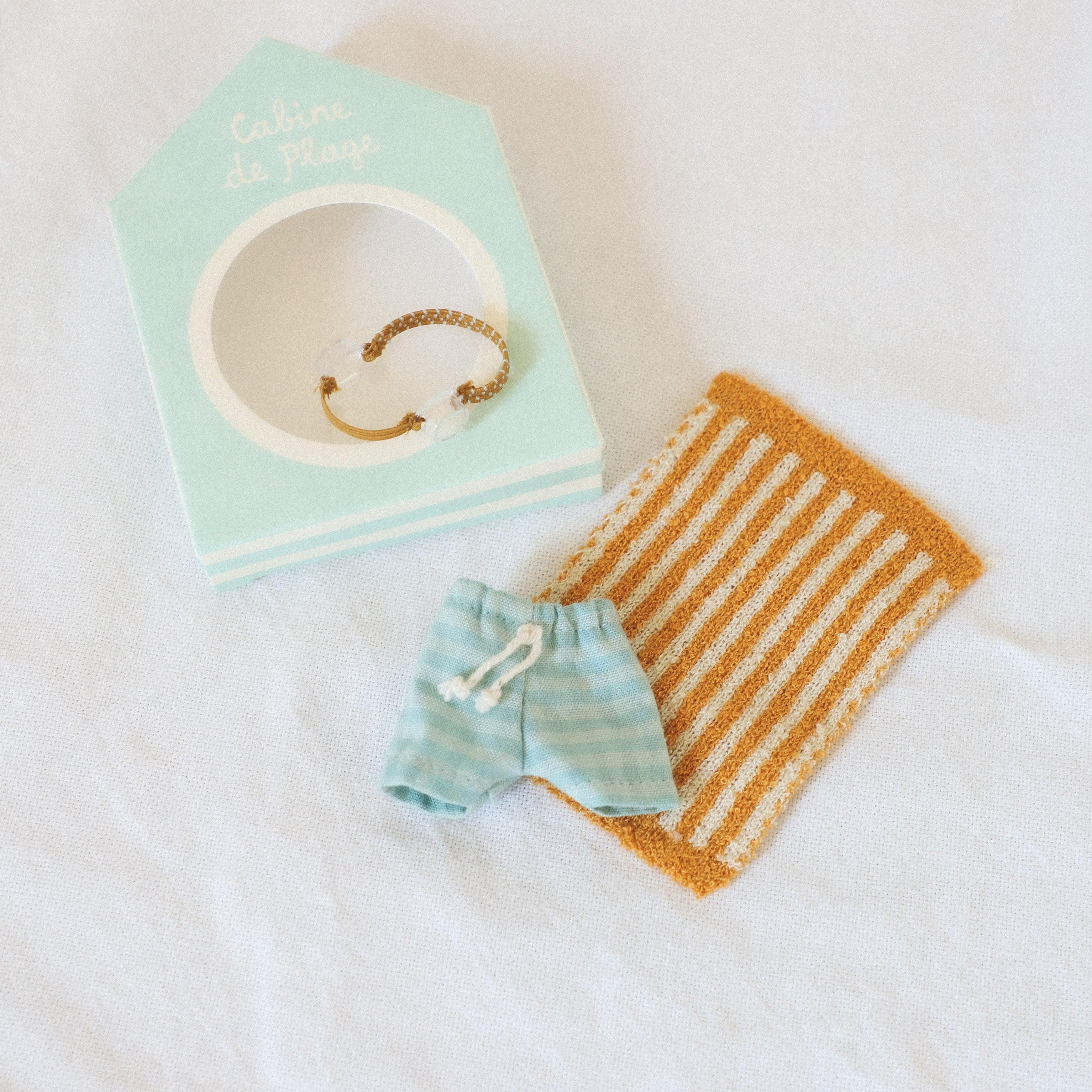Grace & Company Maileg Cabine de Plage Beachset Big Brother: shorts, towel, bracelet, and beach hut box on white fabric.