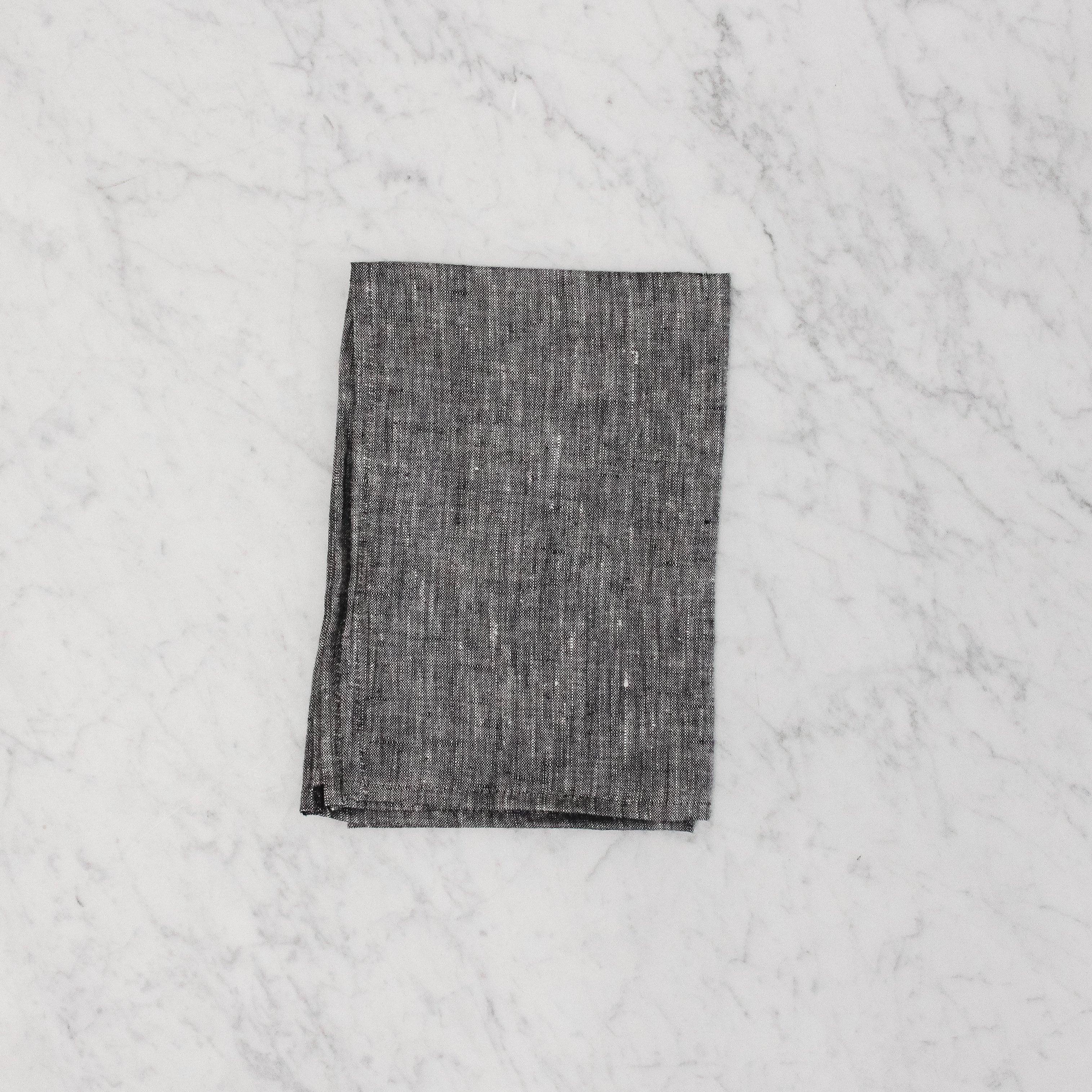 A G&C - Tea Towel by Grace & Company ltd, folded dark gray, on a white marble surface.