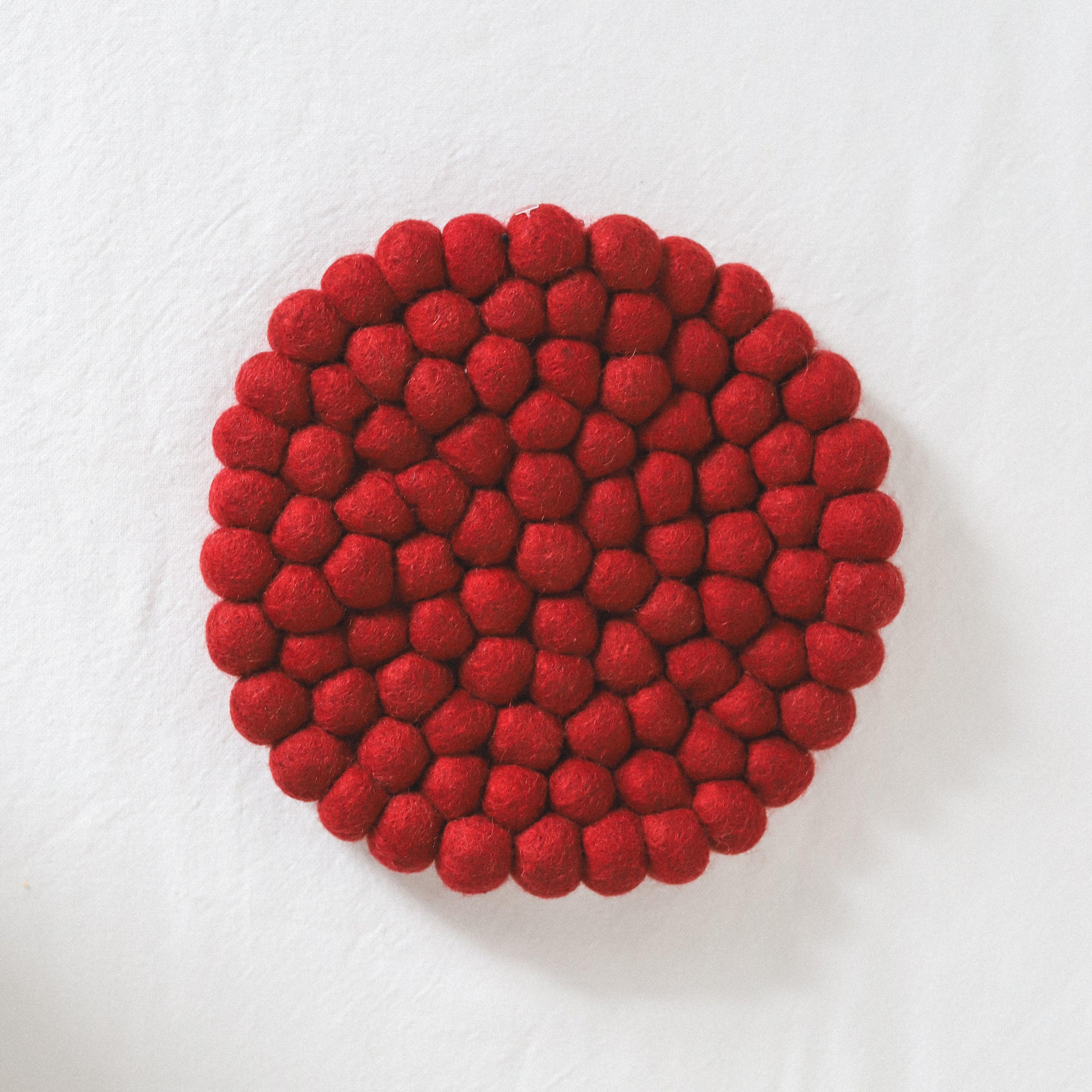 A round mat made of clustered red felt balls on a white background.