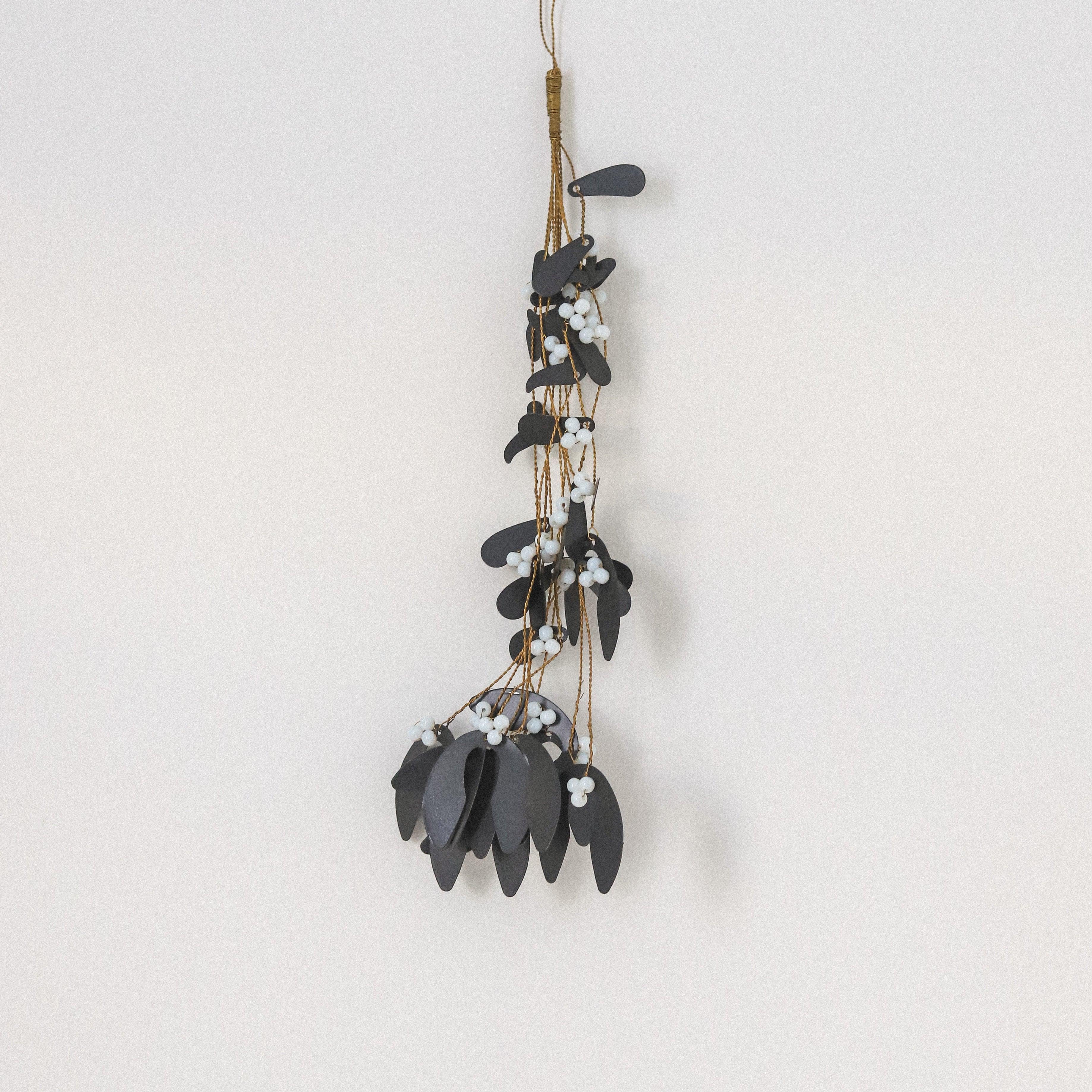 The Ornament - Mistletoe Black by Grace & Company features dark leaves and white berries on a light wall.