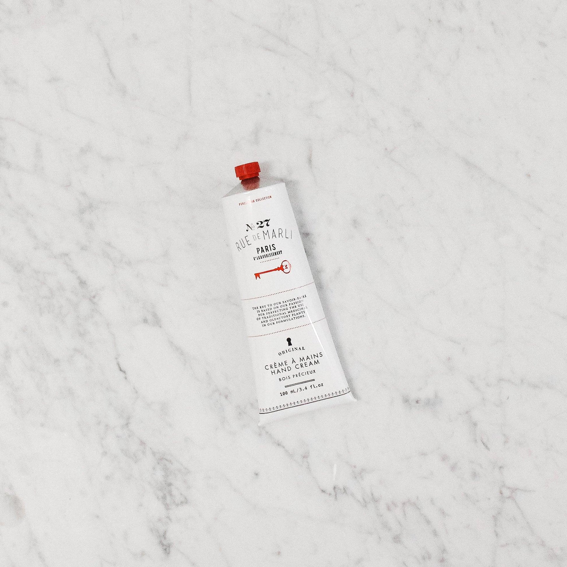 The Rue de Marli No. 27 Hand Cream by Grace & Company ltd rests on a white marble surface.