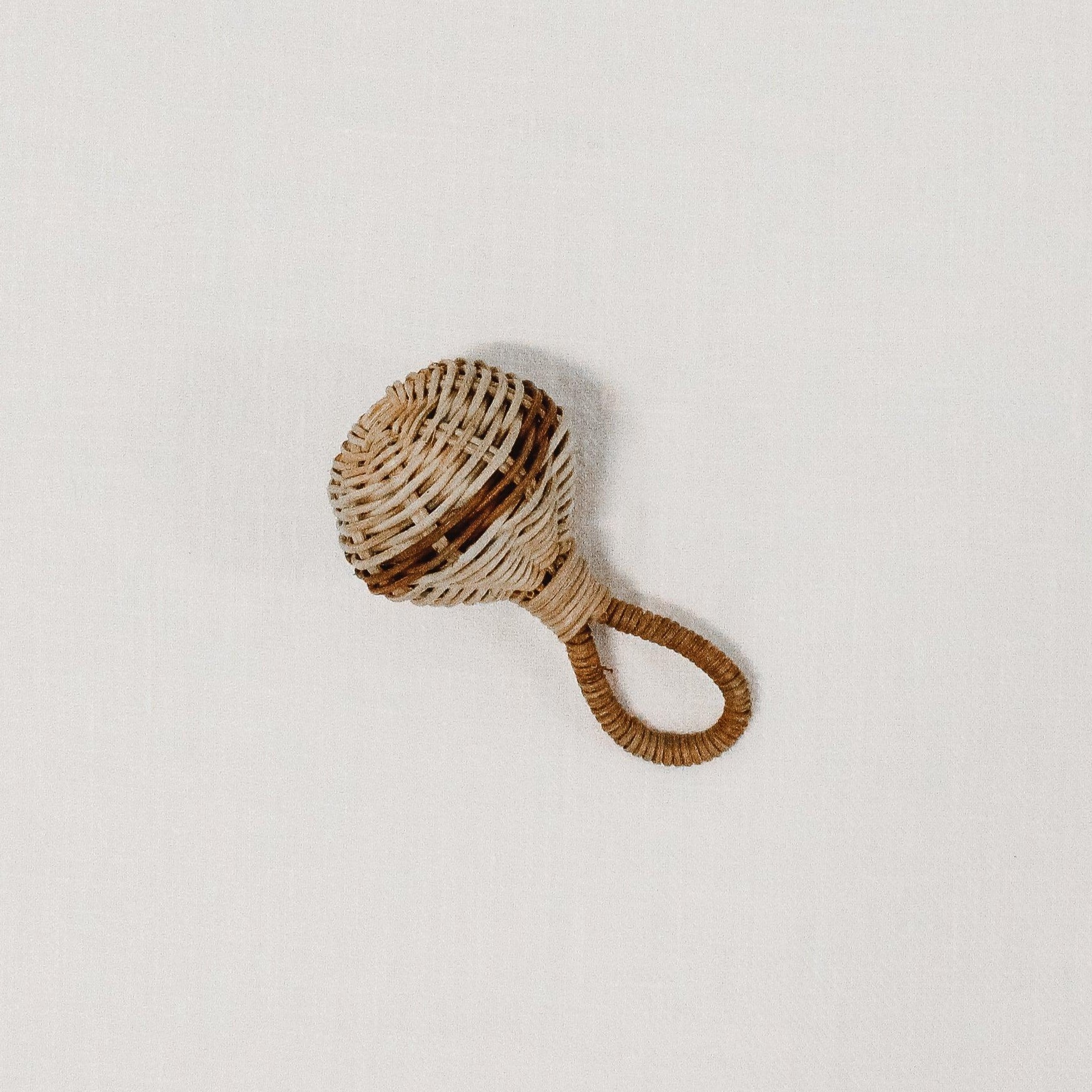 The Olli Ella - Raya Rattle by Grace & Company is a small rattan baby rattle with a round top and looped handle.