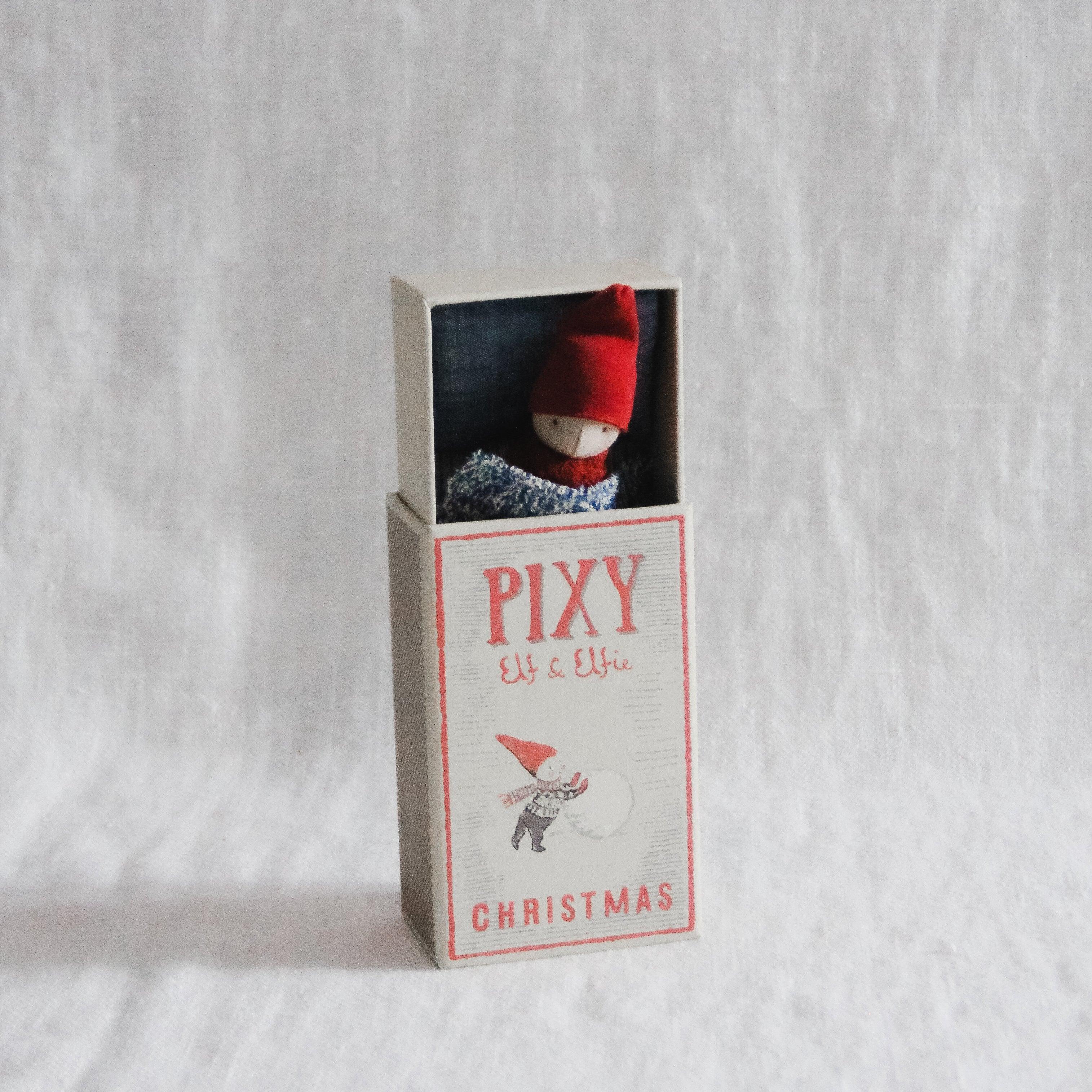 A Maileg - Pixy Elf in a Box by Grace & Company peeks from its box against a white fabric background.