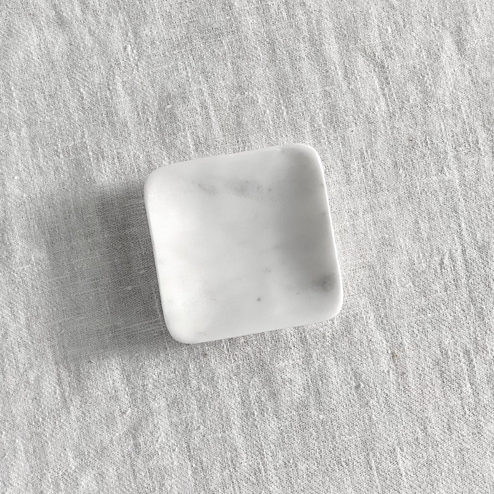 The Grace & Company Square Marble Soap Dish rests on a textured light gray fabric surface.