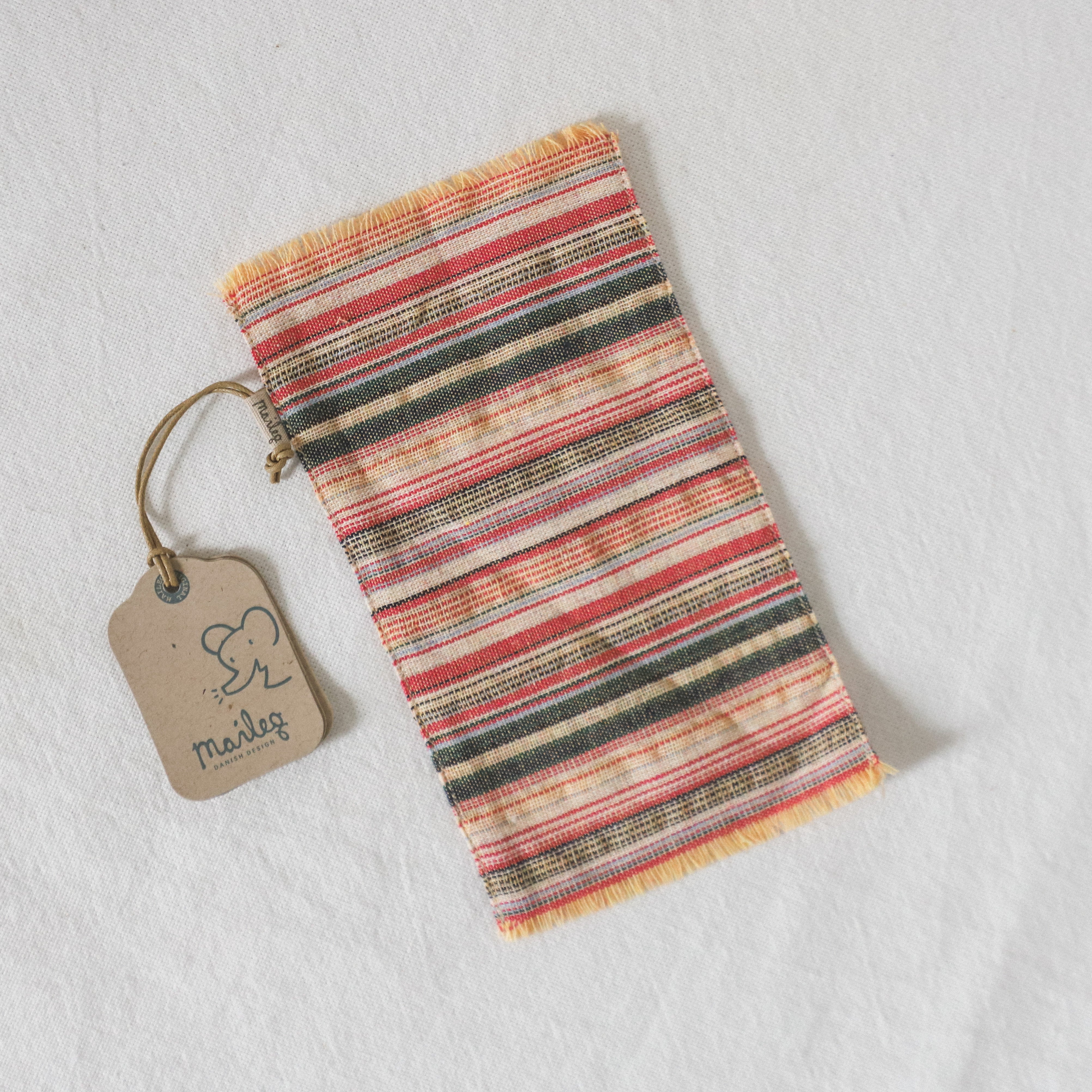The Maileg - Striped Rug by Grace and Company Ltd, featuring a brown mudag tag, rests on a white surface.