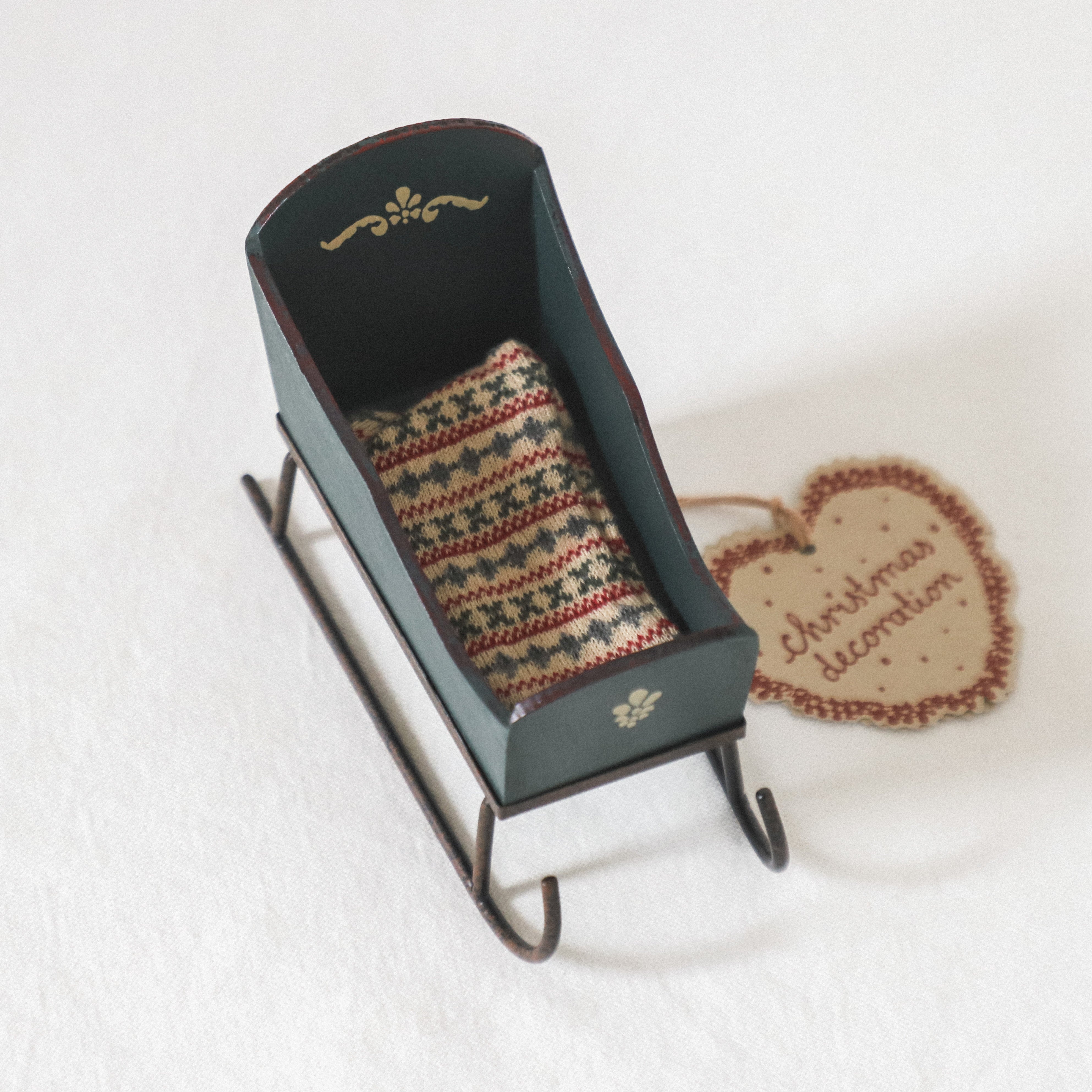 The Maileg - Holiday Sleigh by Grace and Company Ltd features a patterned cushion and a heart-shaped Christmas tag.
