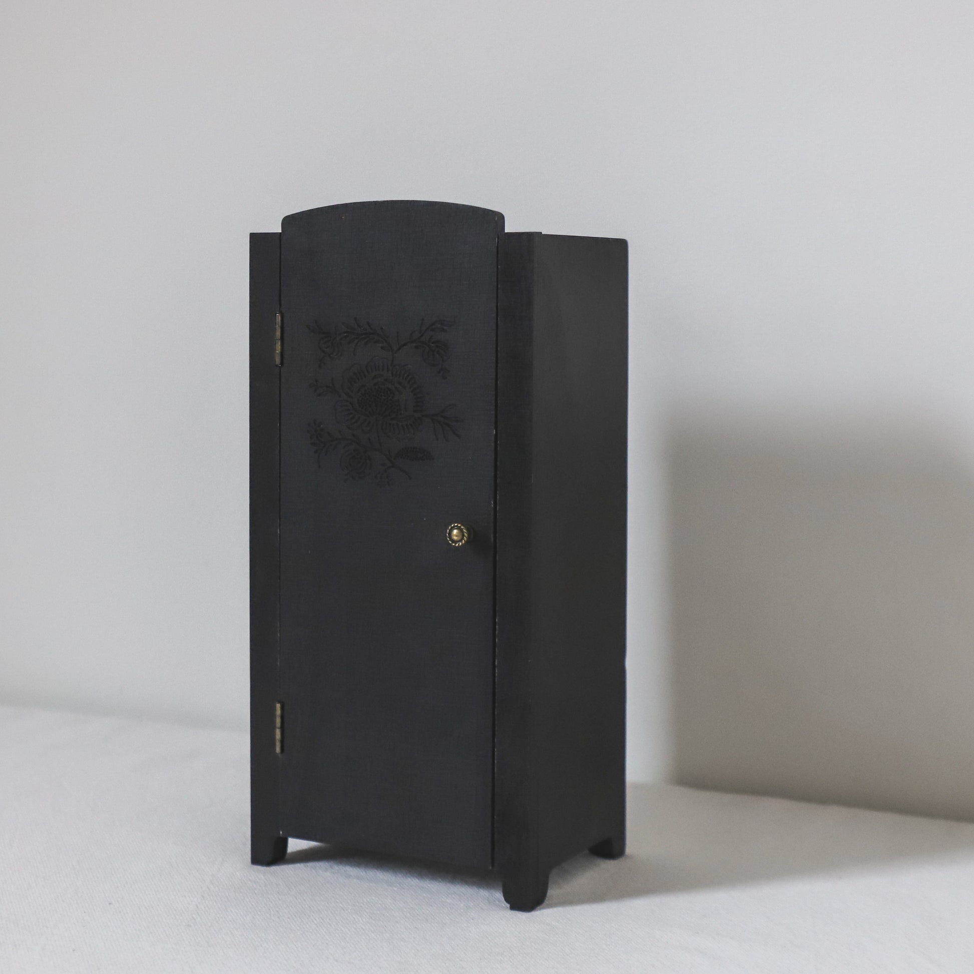 The Maileg Classic Wooden Wardrobe by Grace and Company Ltd is a small black cabinet with a floral door, on white surface.