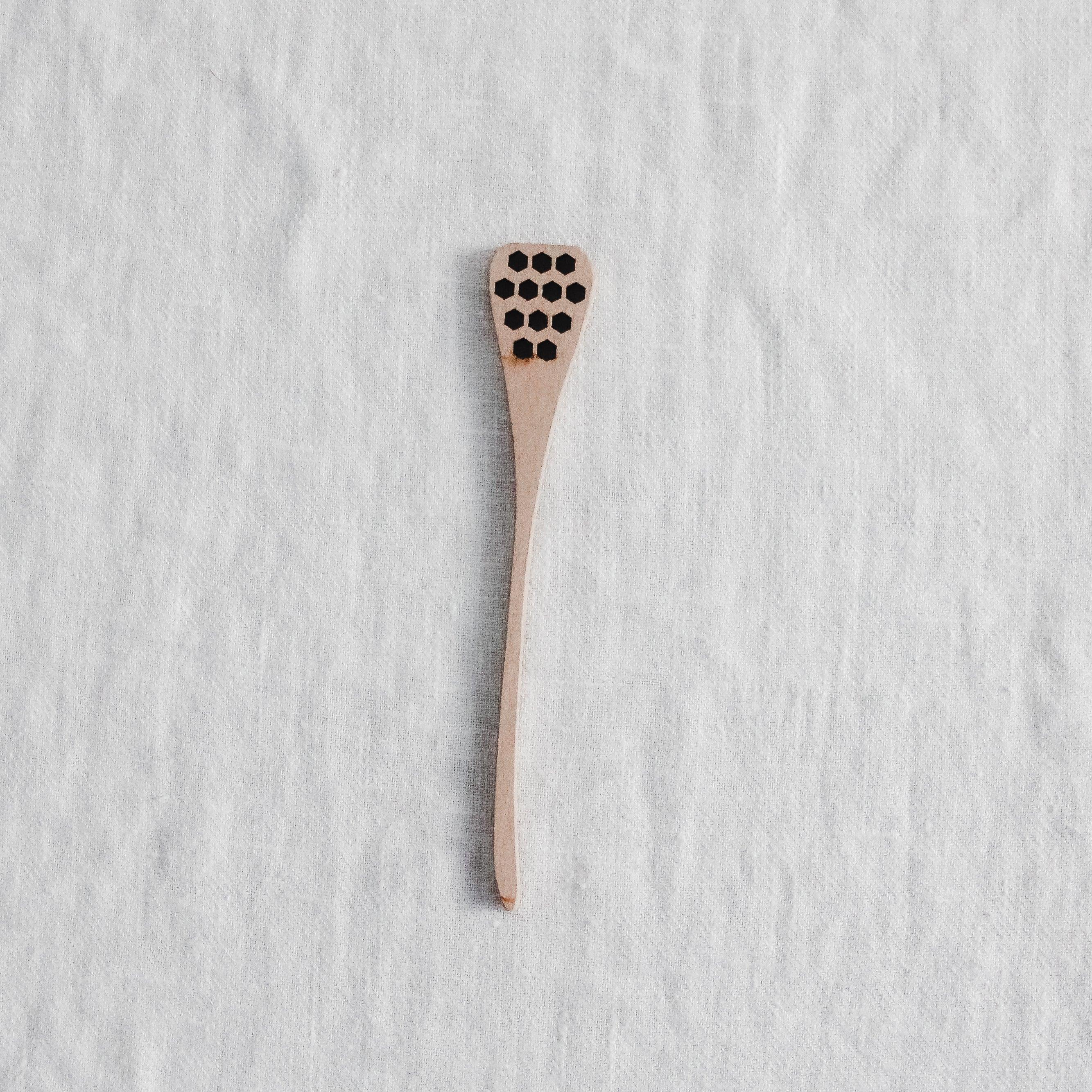 The Grace & Company ltd Honey Spoon rests on textured white fabric.