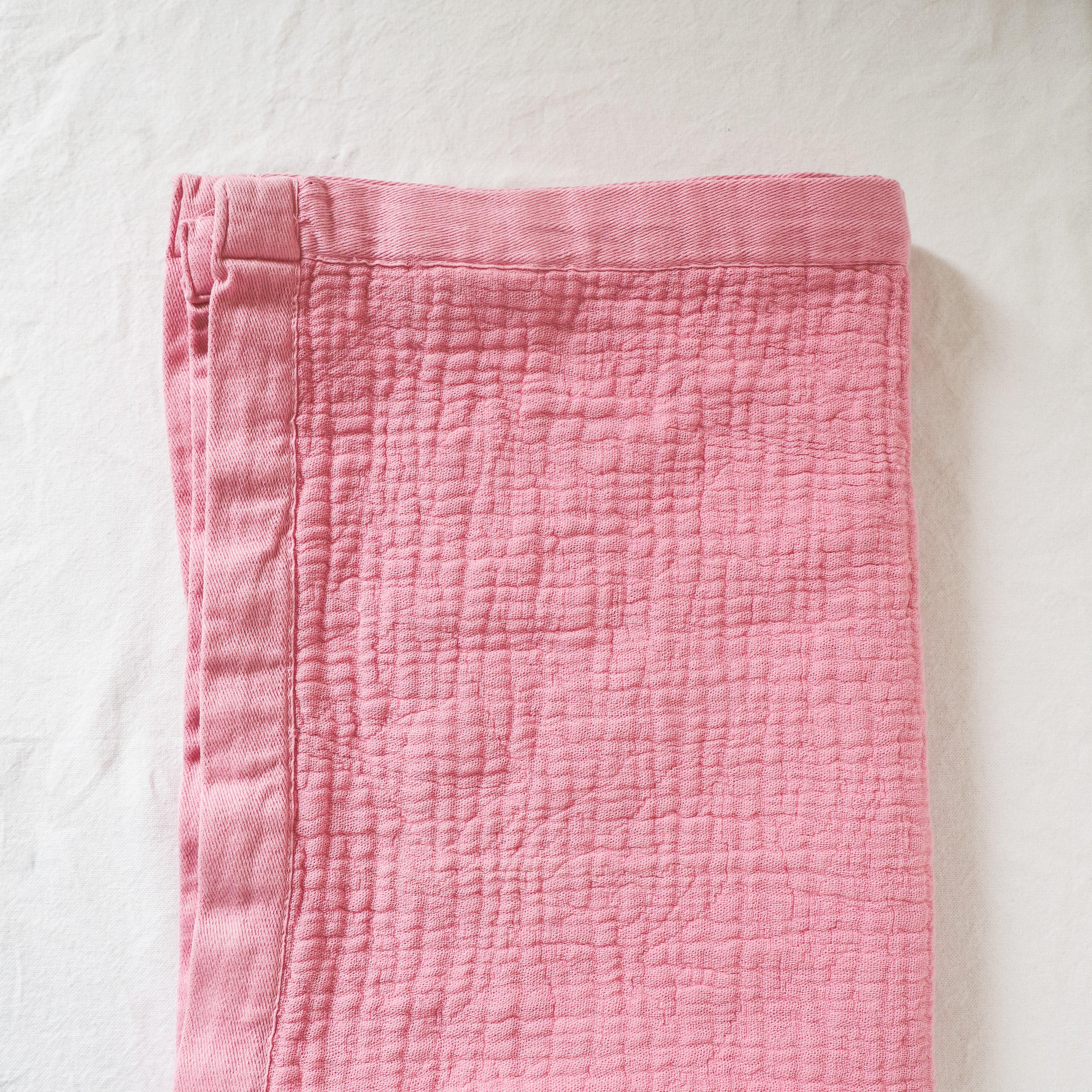 The Linen Way - Porto Baby Blanket by Grace & Company ltd, folded in pink, rests on a white surface.