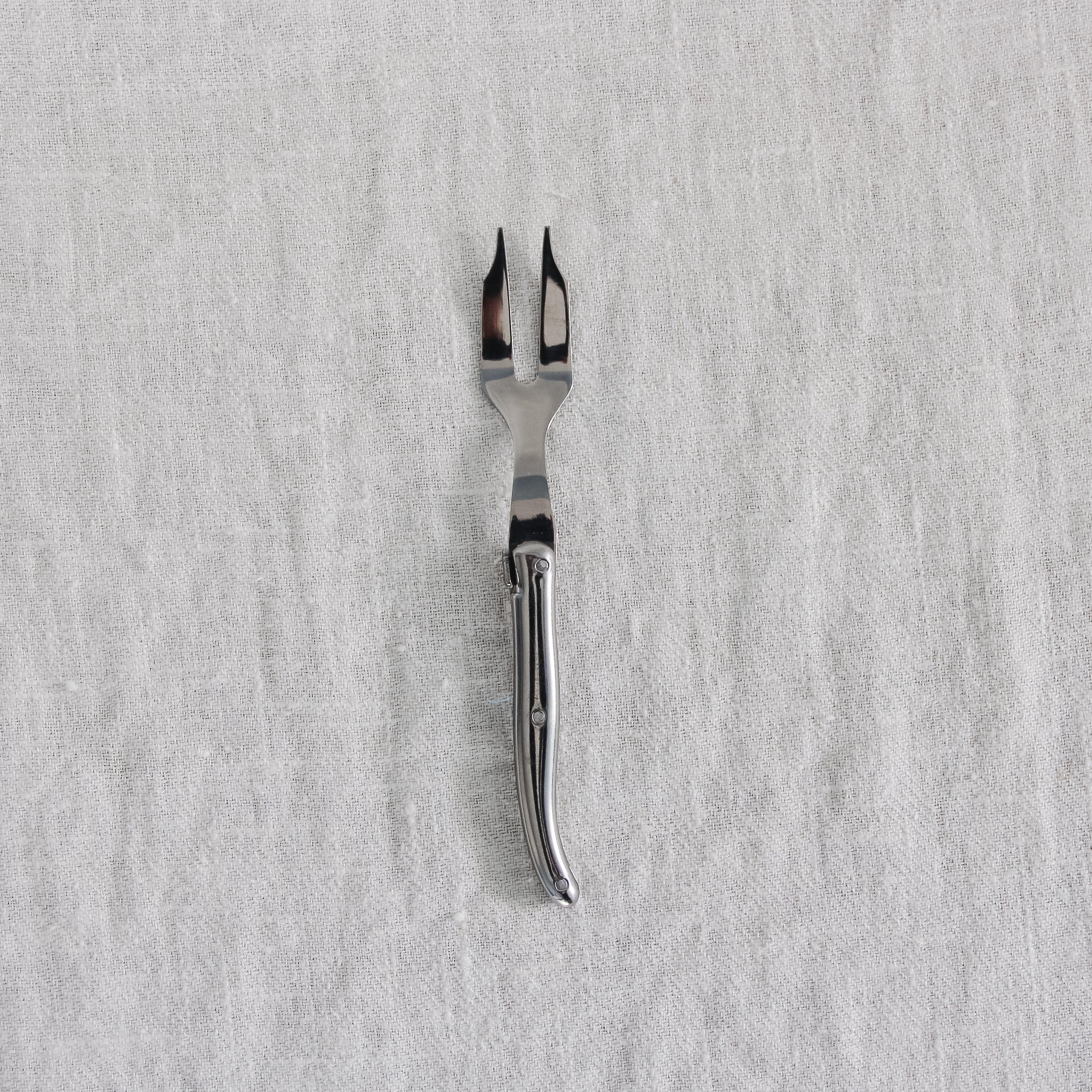 The Grace & Company Vintage Fork has two prongs and rests on a light gray textured fabric background.