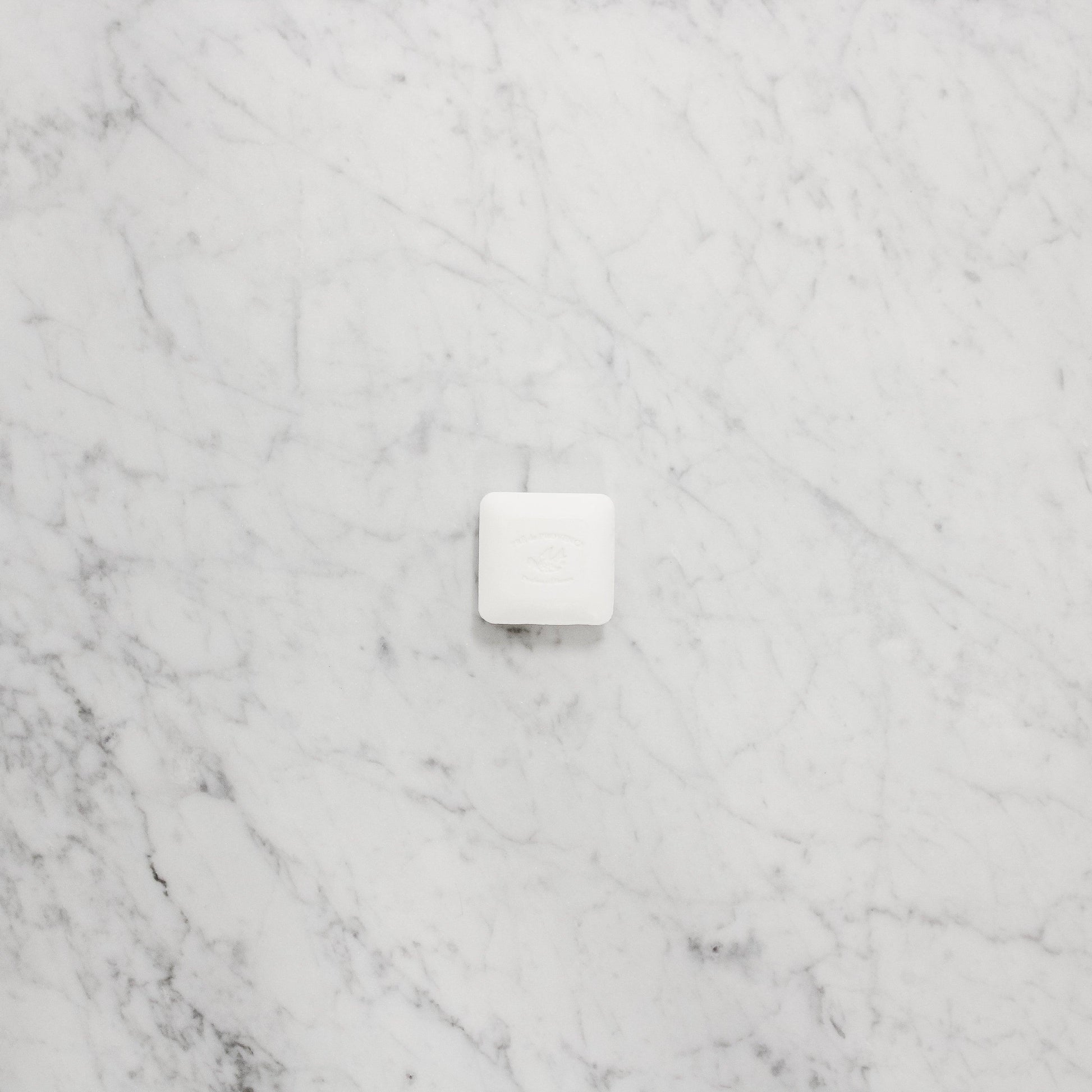 A Pre de Provence Mini Soap - Lait by Grace & Company ltd sits on a light gray marble surface.