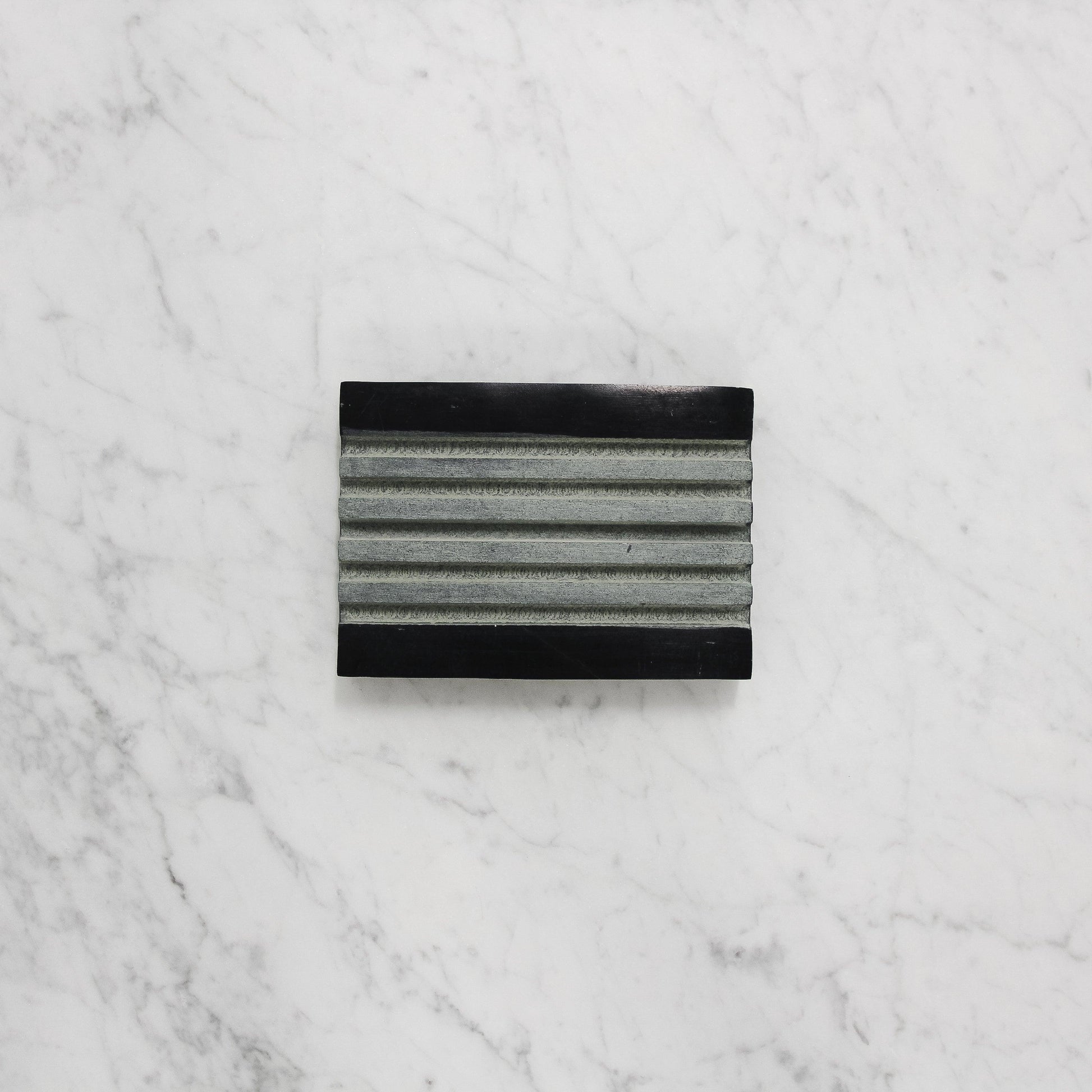 The Grace & Company ltd Lothantique Tadé Black Marble Soap Dish with grooves sits on a white marble surface.