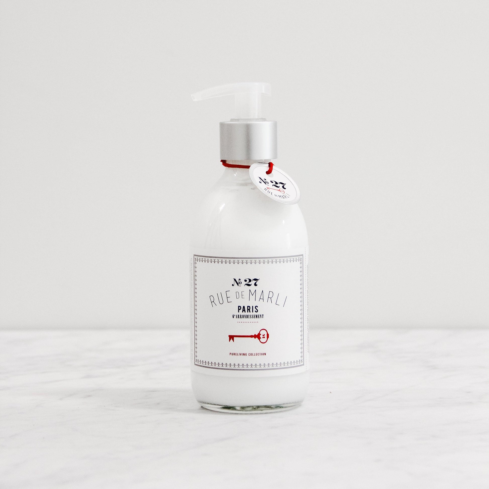 Rue de Marli No. 27 Body Lotion by Grace & Company Ltd in a clear pump bottle on a white marble surface.