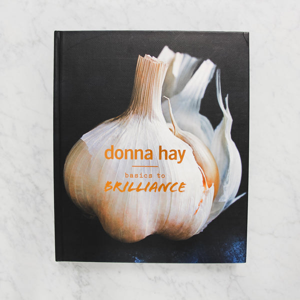 front cover of donna hay's basics to brilliance. cover depicts a large bulb of garlic against a black background with orange text.