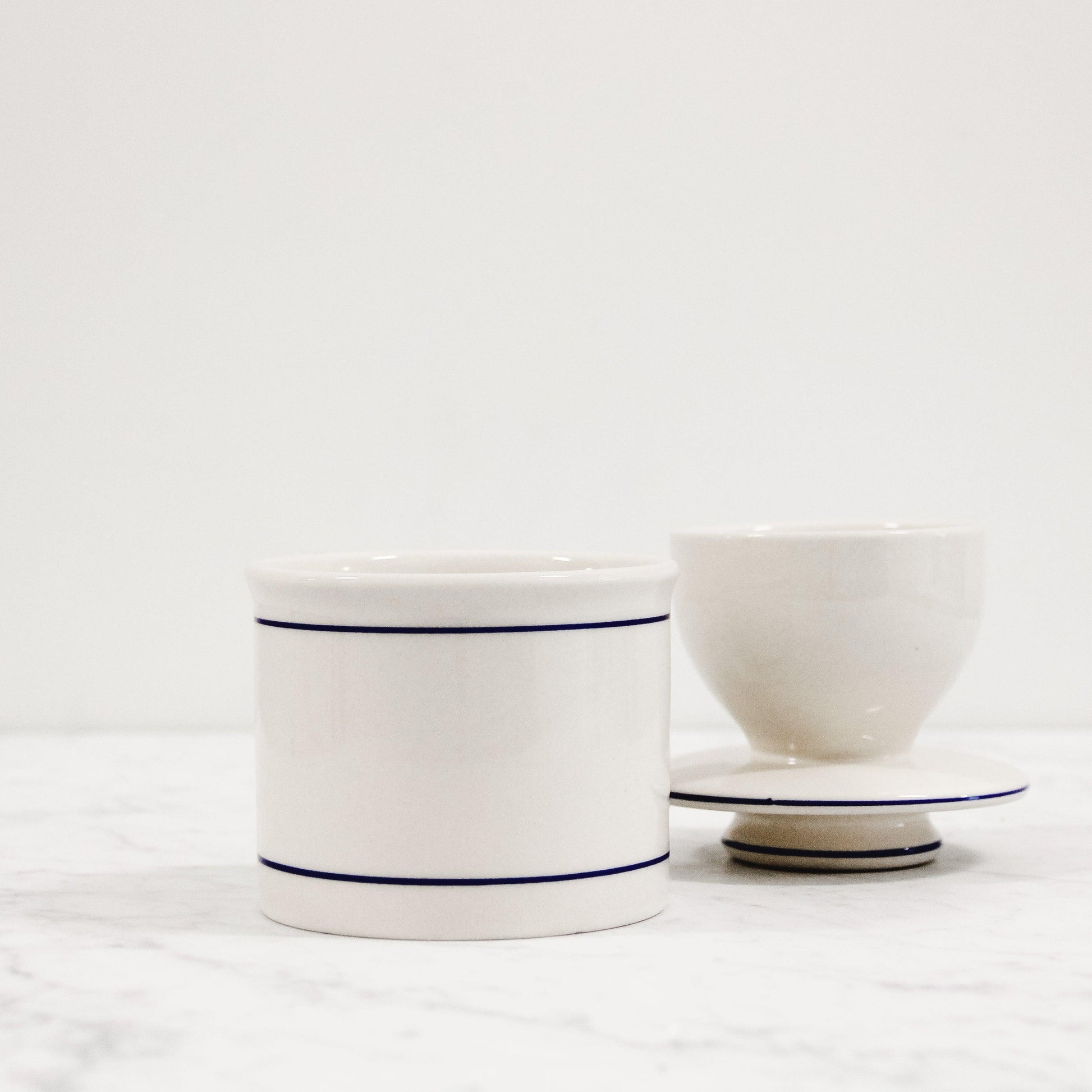 white ceramic butter crock with blue trim. Pictured with lid turned upside down exposing butter compartment.