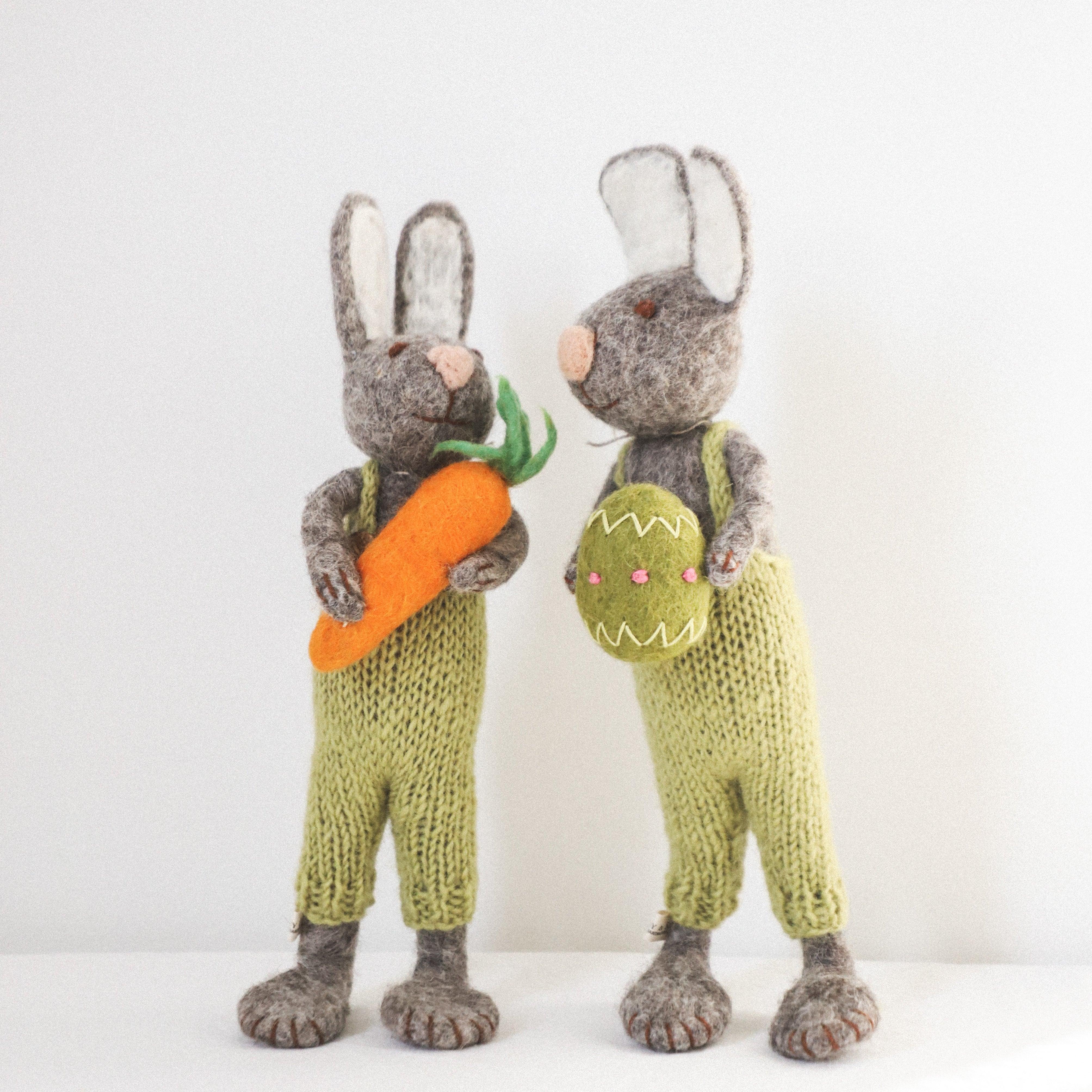 Grace & Company’s Scandi - Woolly Bunnies wear green knits and hold a carrot and egg, standing side by side.