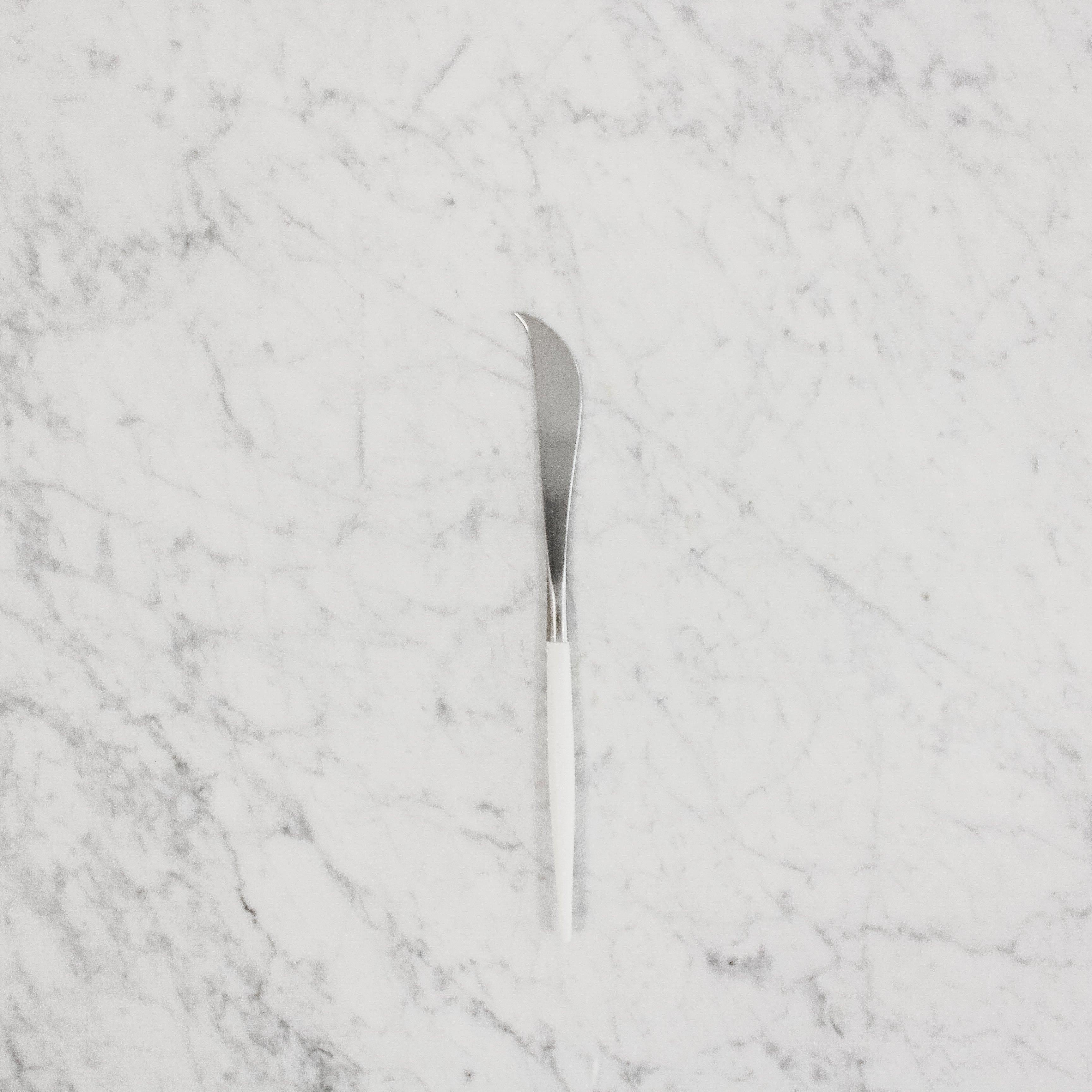 The Cutipol Goa Cheese Knife by Grace & Company ltd with a white handle on a white marble surface.
