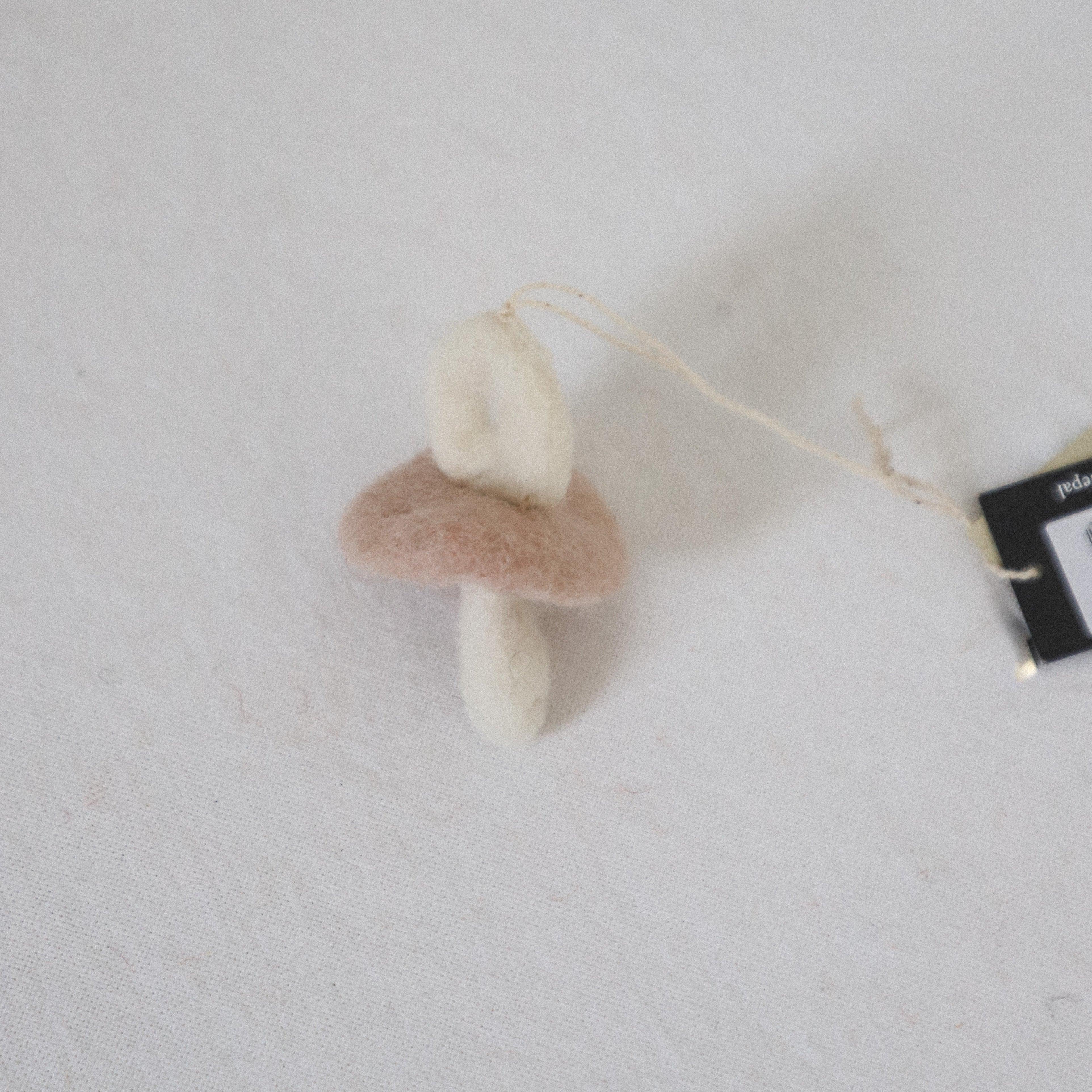 The Grace & Company Scandi-Felted Pacifier ornament with a string rests on a white fabric surface.