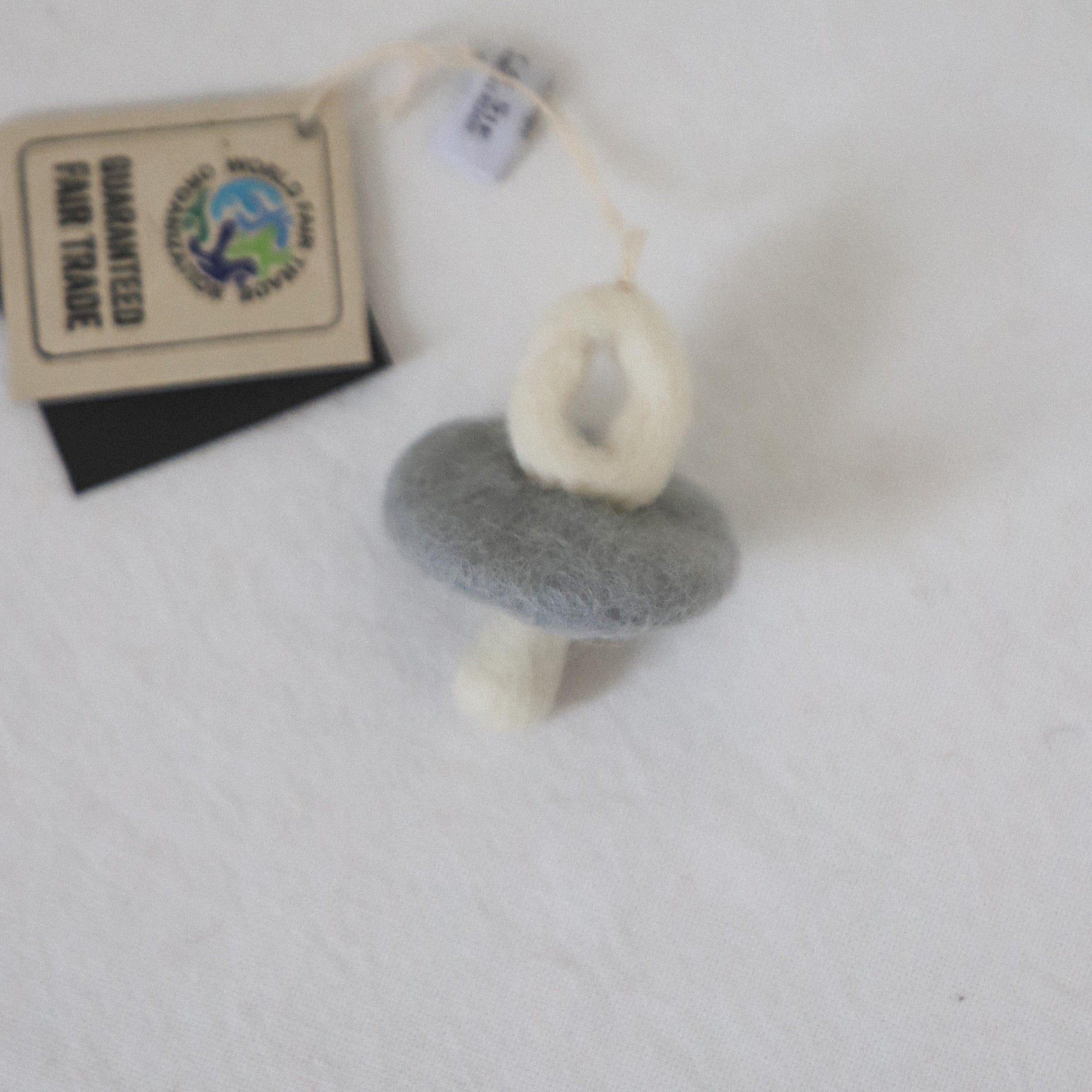 The Scandi -Felted Pacifier by Grace & Company in gray and white with a fair trade tag rests on a white surface.