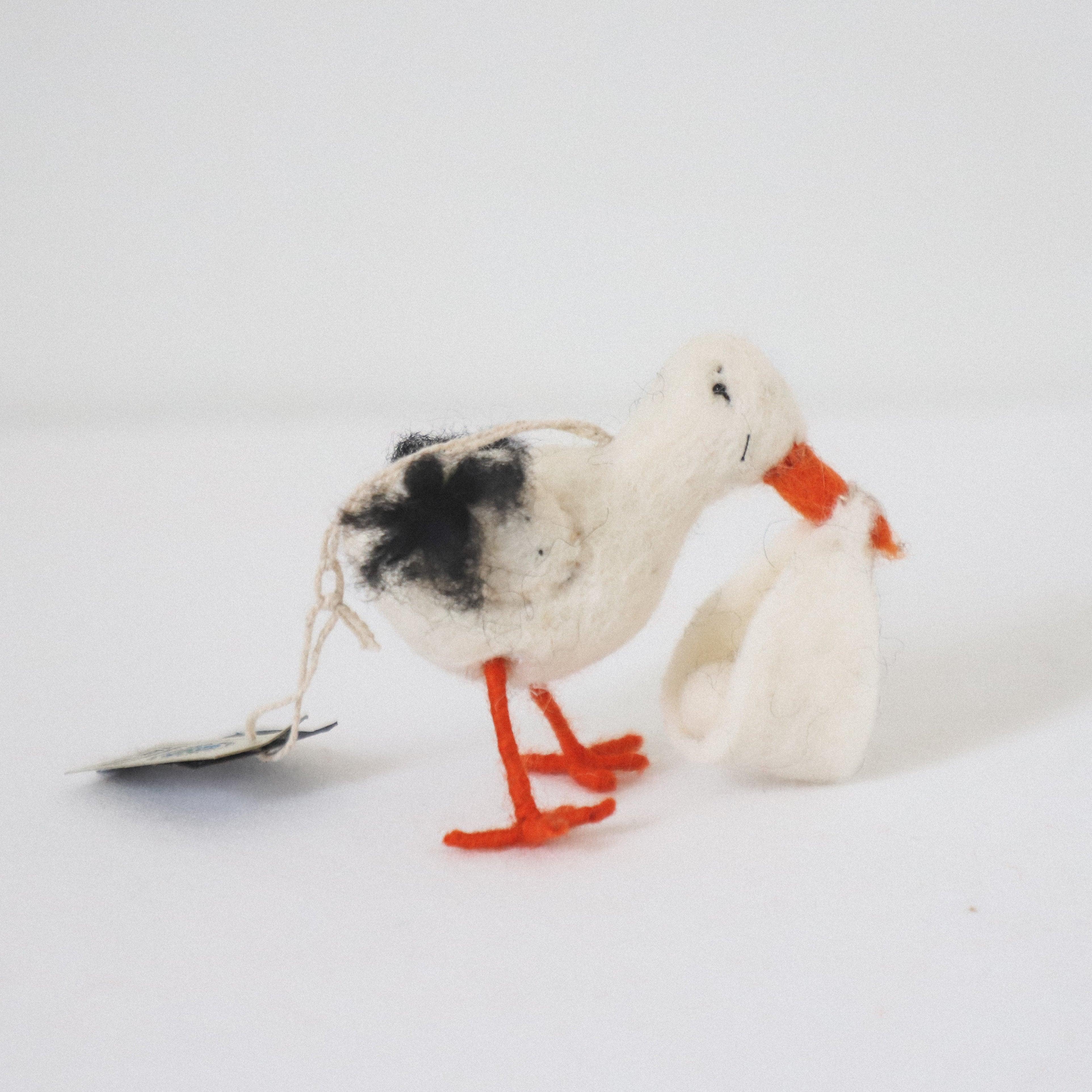 The Scandi Stork Ornament by Grace and Company Ltd features a felt stork with orange legs holding a white bundle.