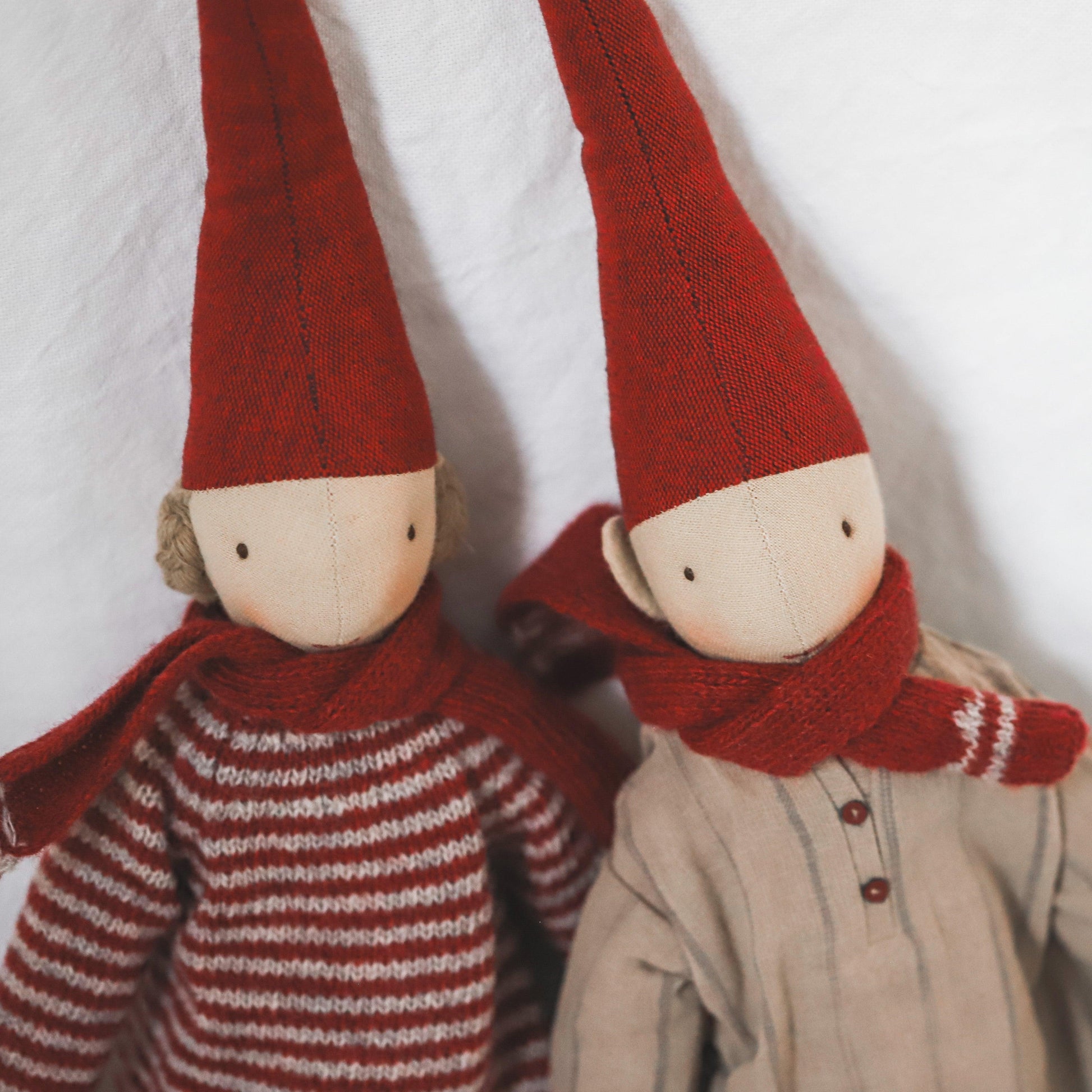 Two Maileg - Pixy Collection dolls by Grace & Company with tall red hats and scarves, striped and beige, on white background.