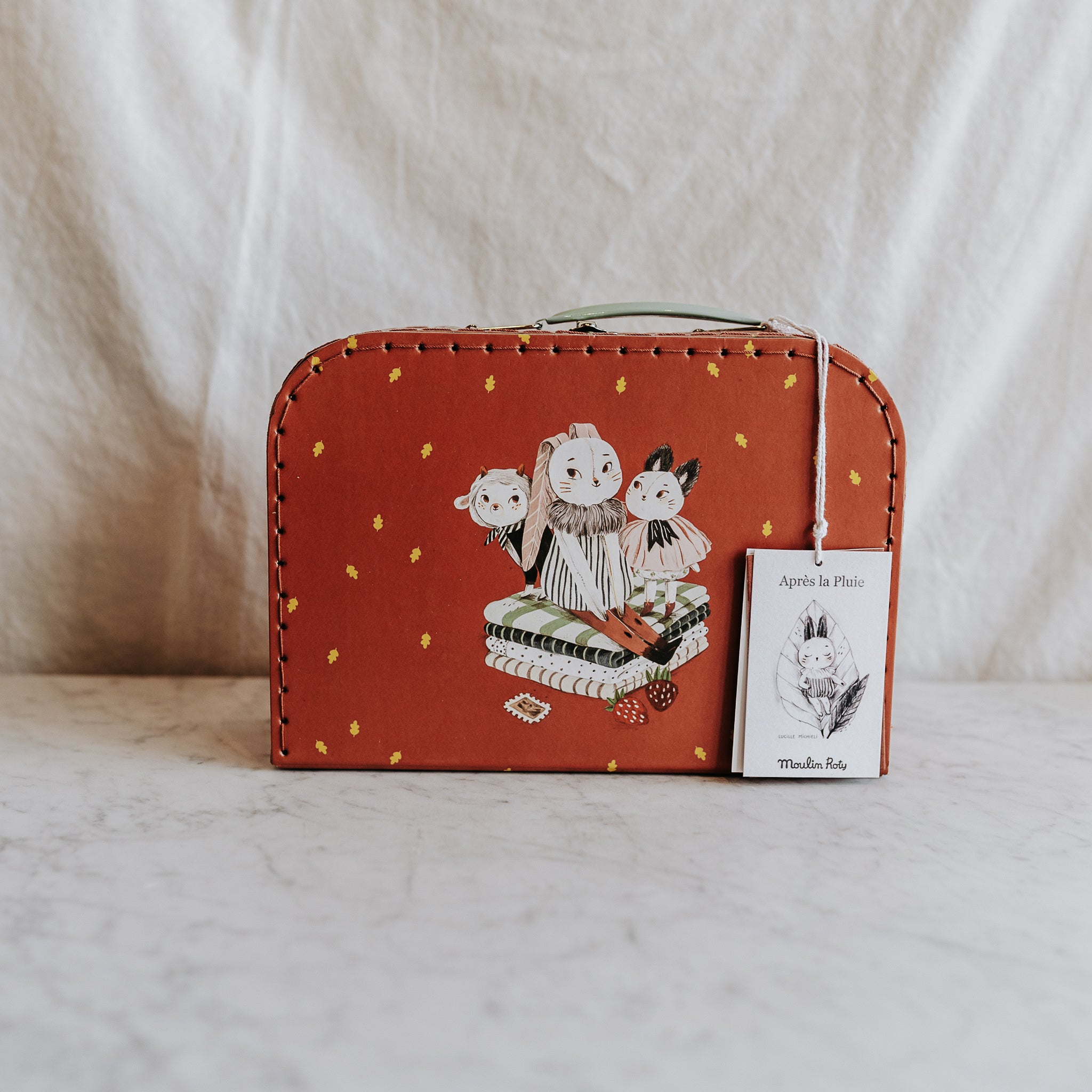 The Moulin Roty - Apres la Pluie suitcase by Grace & Company features animal designs and rests on a marble surface.