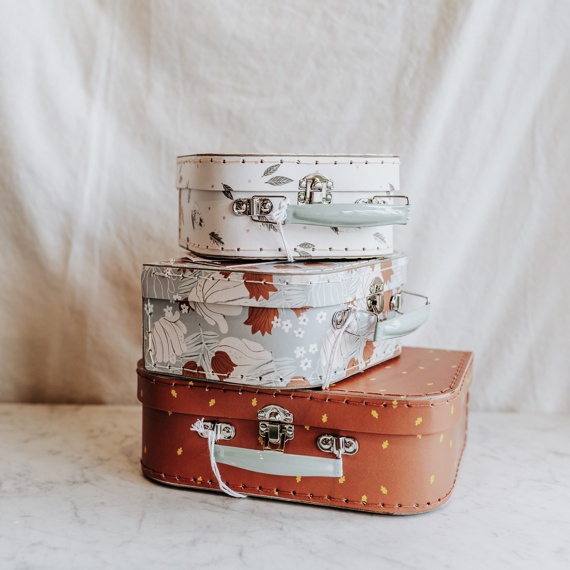 Moulin Roty Apres la Pluie suitcases by Grace & Company, stacked with floral and dot prints on a marble surface.