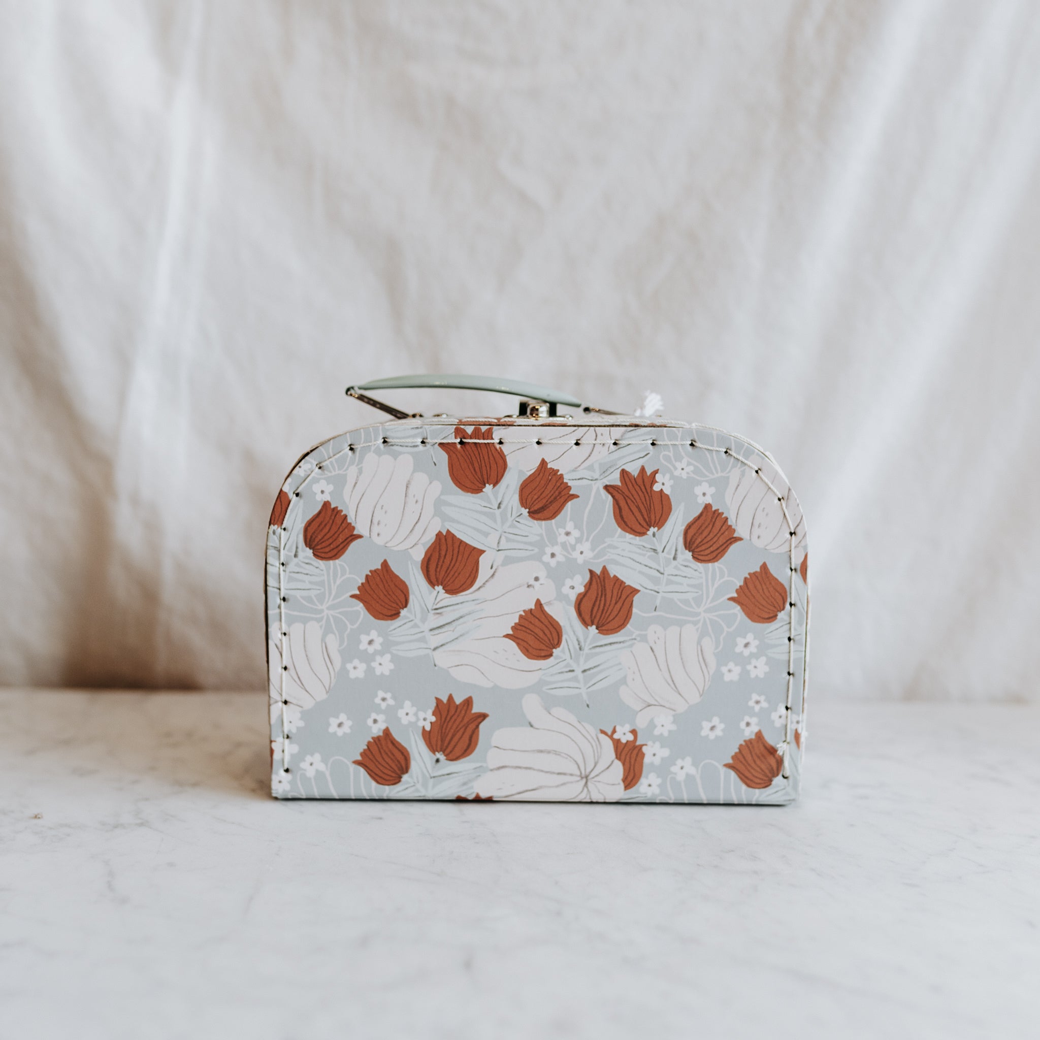 Moulin Roty - Apres la Pluie suitcase by Grace & Company in white and rust floral on light blue, shown on marble.