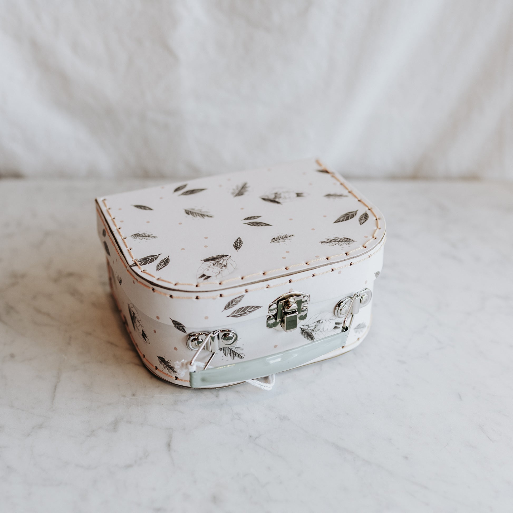 Moulin Roty Apres la Pluie suitcase by Grace & Company—white with feather pattern, silver latch, light green handle.