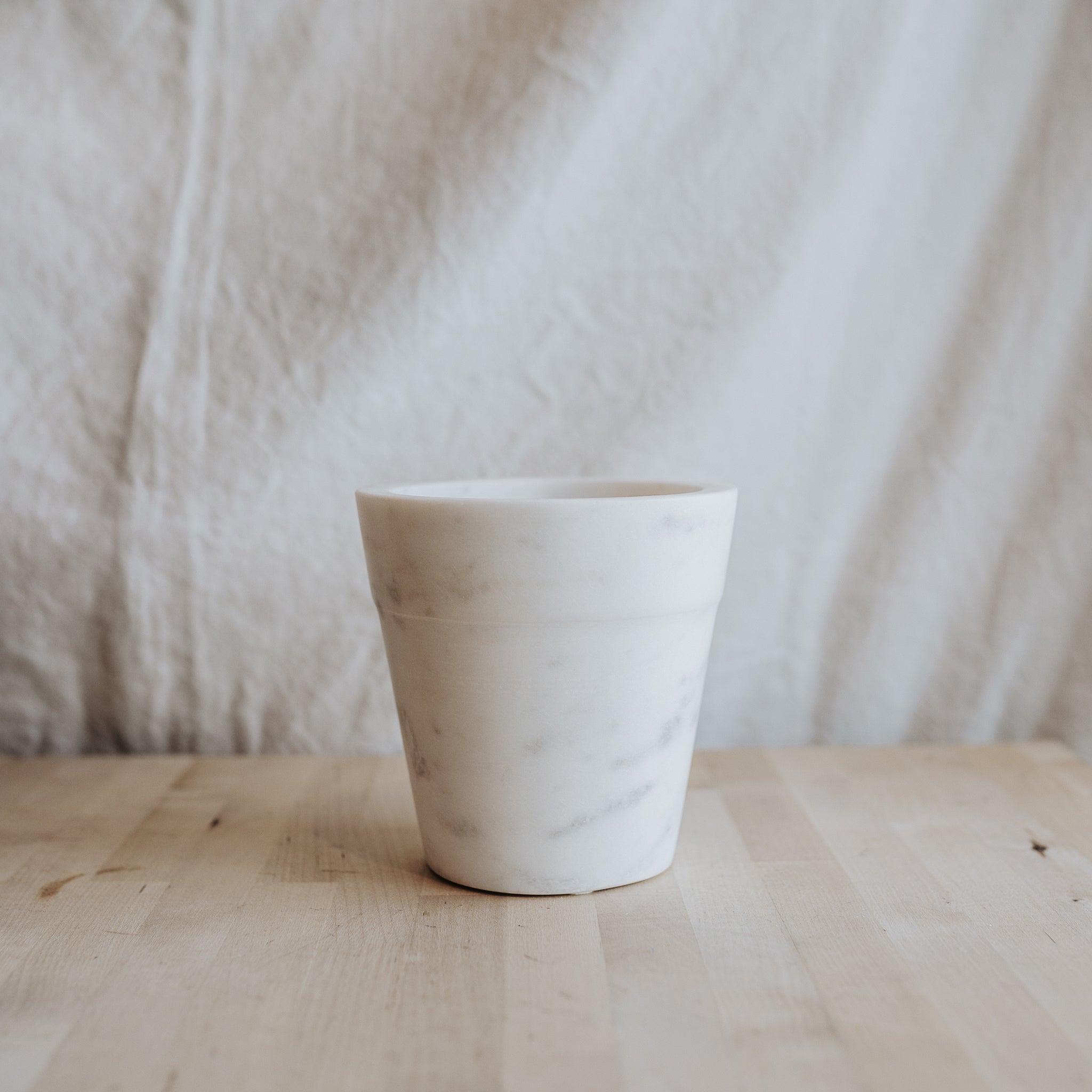 The Grace & Company Marble Flower Pot sits on a light wood surface with a neutral fabric background.