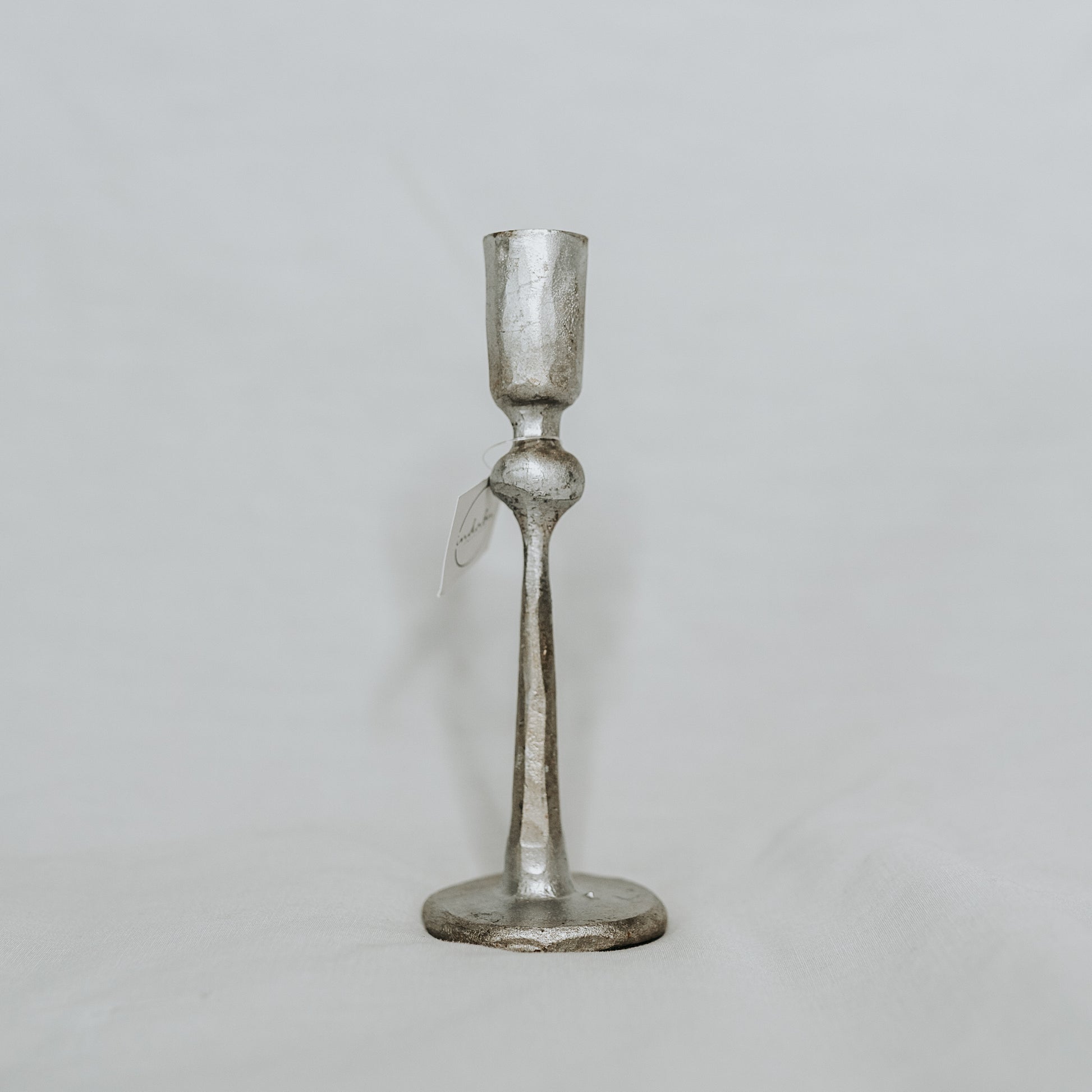 Grace & Company Canmore Taper Candle Holder in silver, shown with tag on a plain white background.